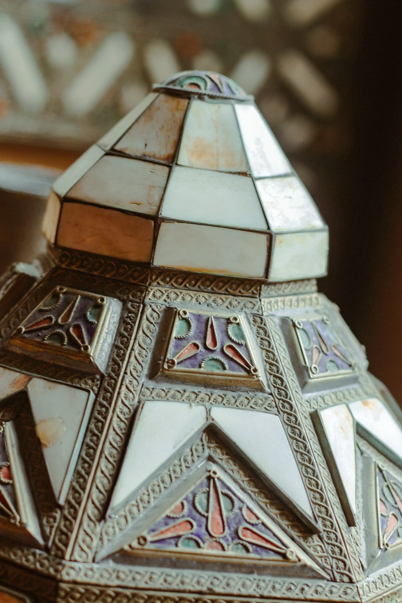 Une lampe en mosaïque en forme de dôme décoré de morceaux de coquillage ou de céramique colorés et de détails métalliques.