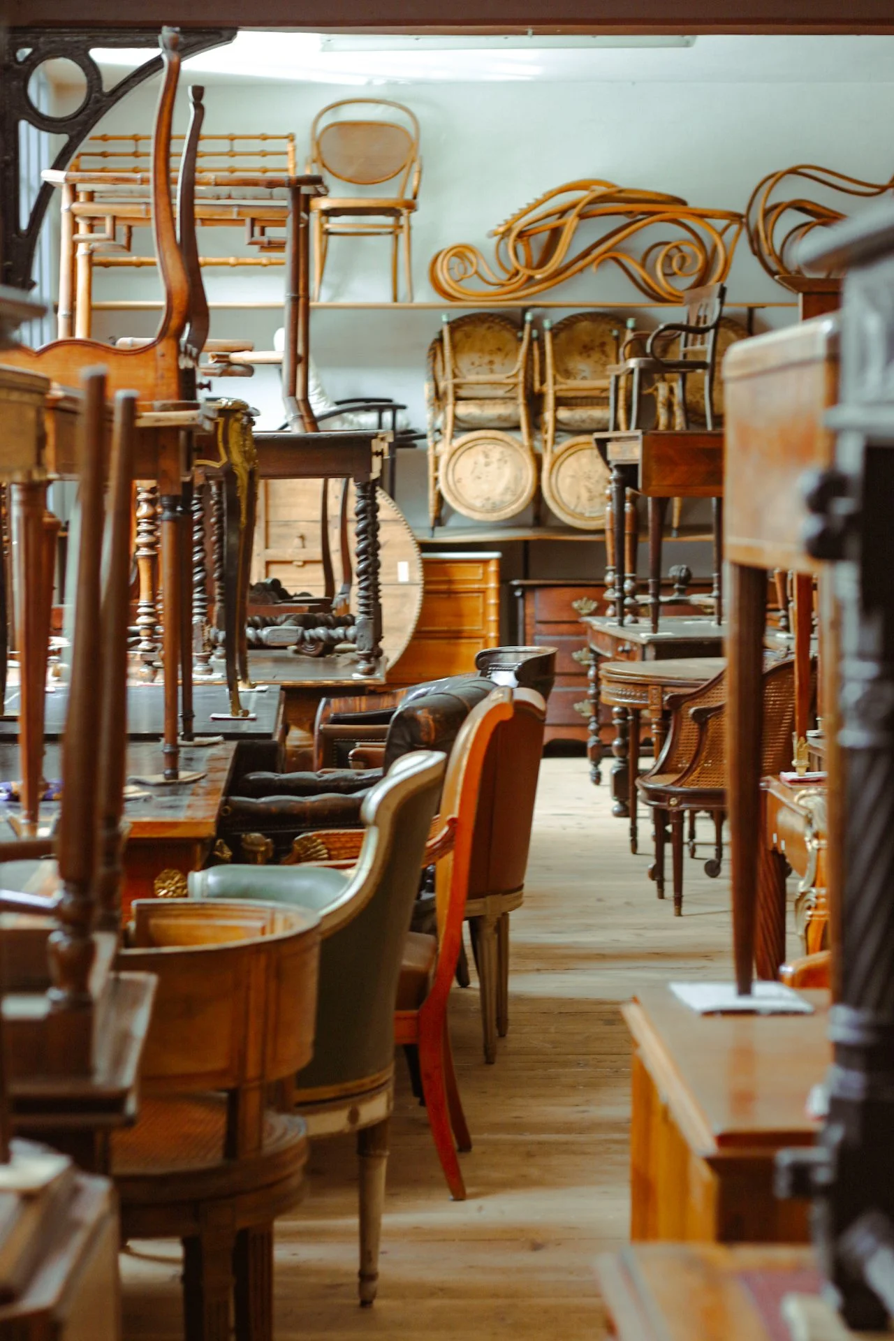 Un entrepôt rempli de meubles en bois, notamment des chaises, des tables et des étagères, empilés et rangés en hauteur.