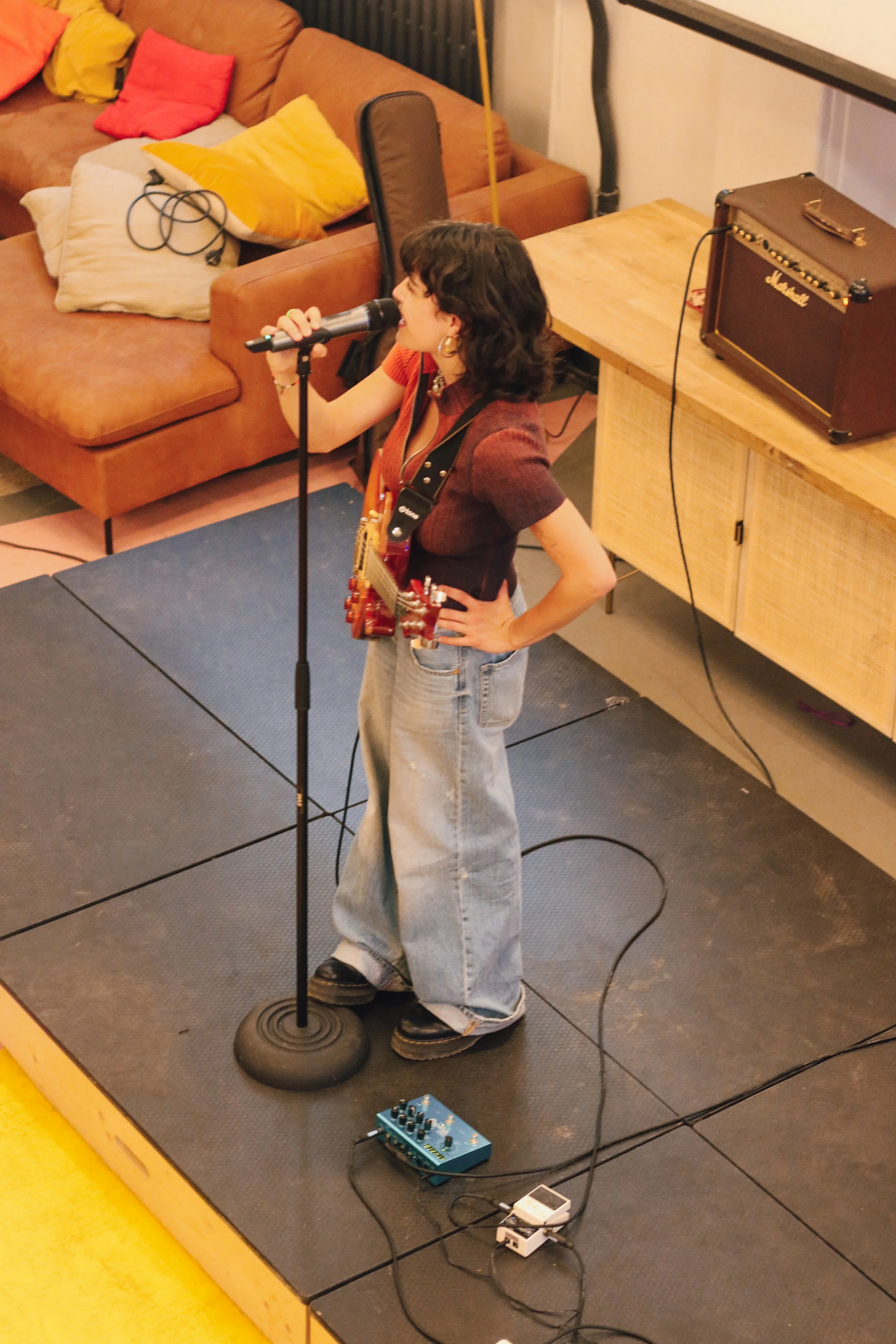 Une femme avec une guitare, chantant dans un micro sur une petite scène intérieure.