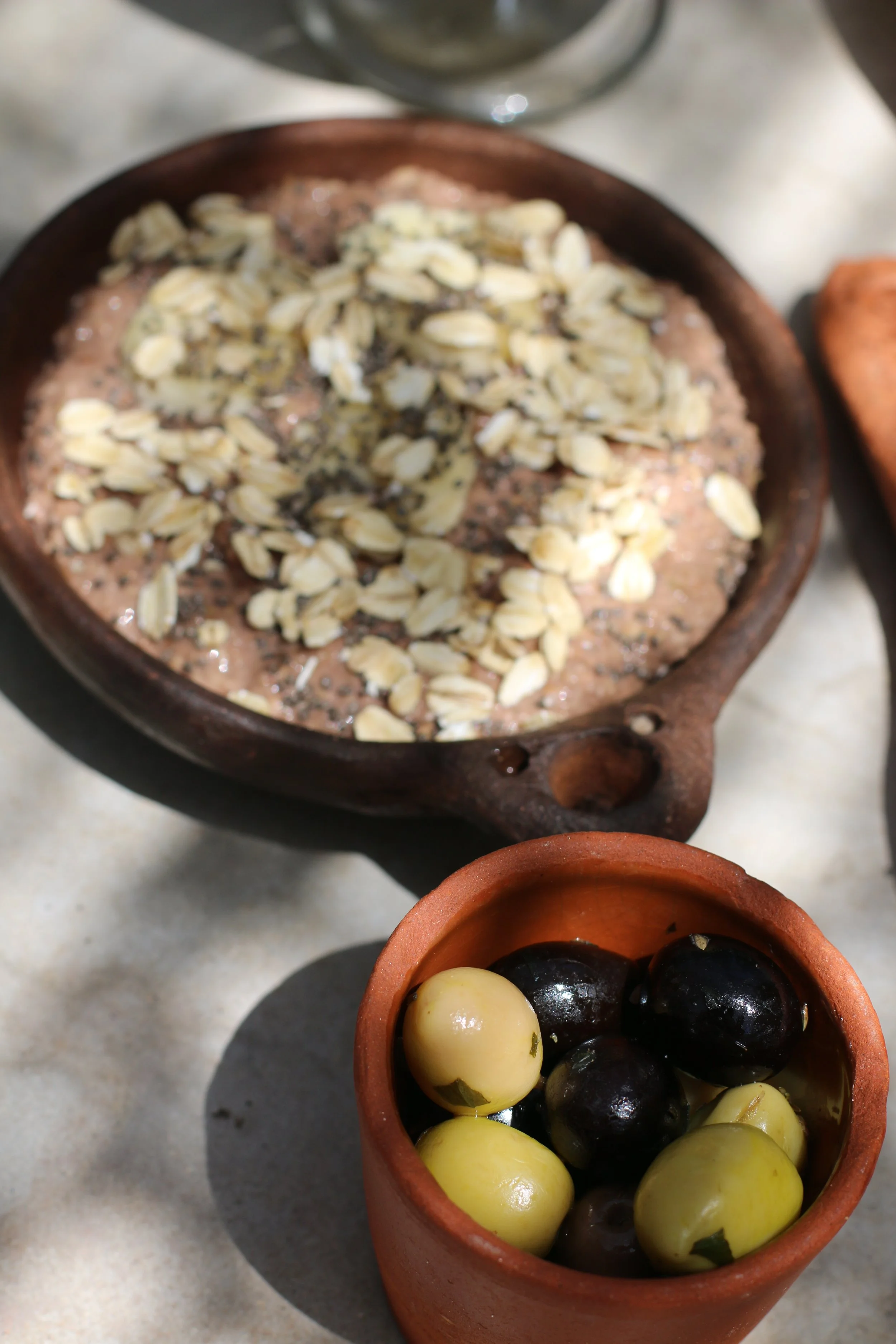 Bol à fleurette avec de l'avoine, trempée dans l'eau, accompagnée d'un pot avec des olives vertes et noires.