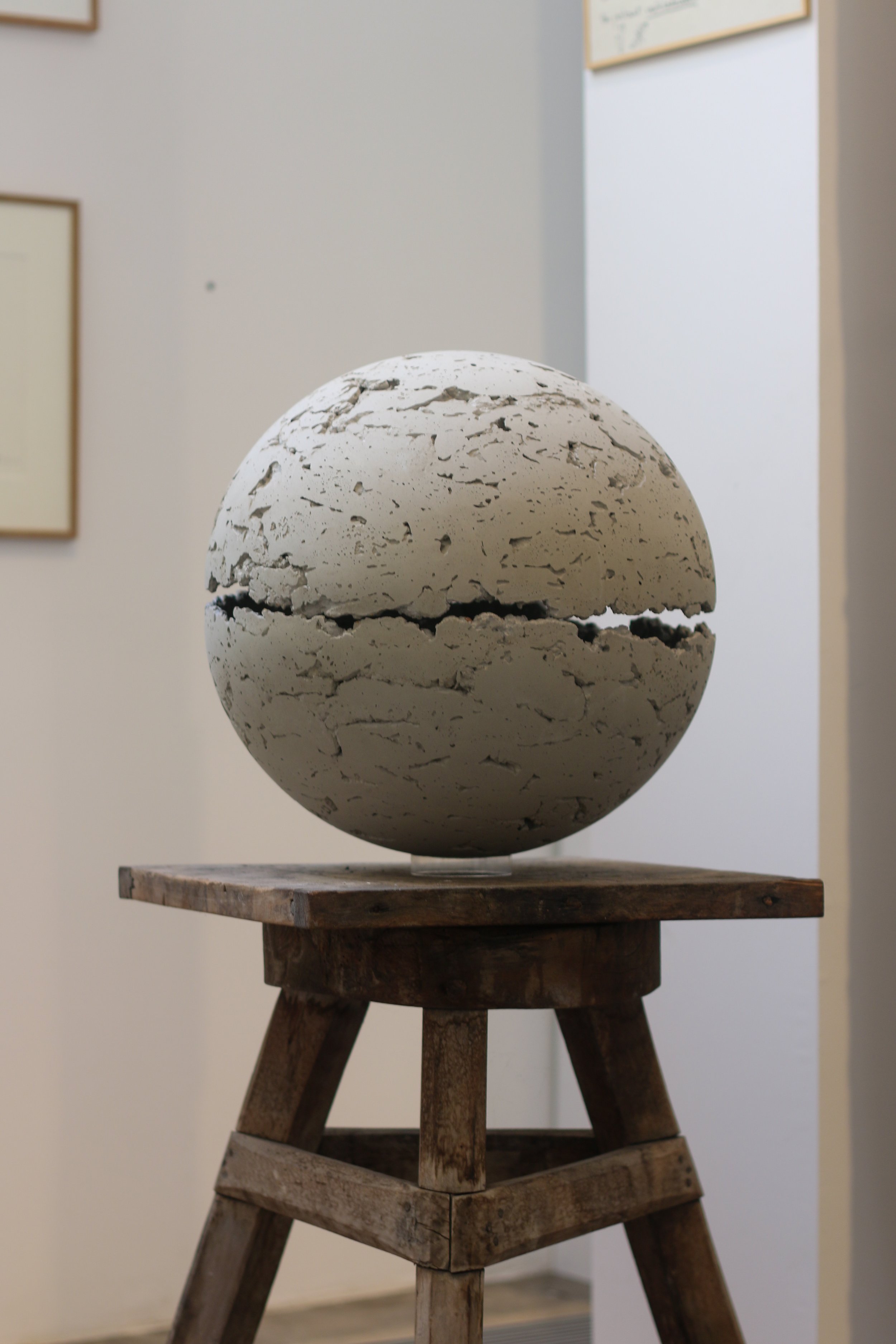 Sculpture en forme de sphère fissurée, posée sur une table en bois rustique.