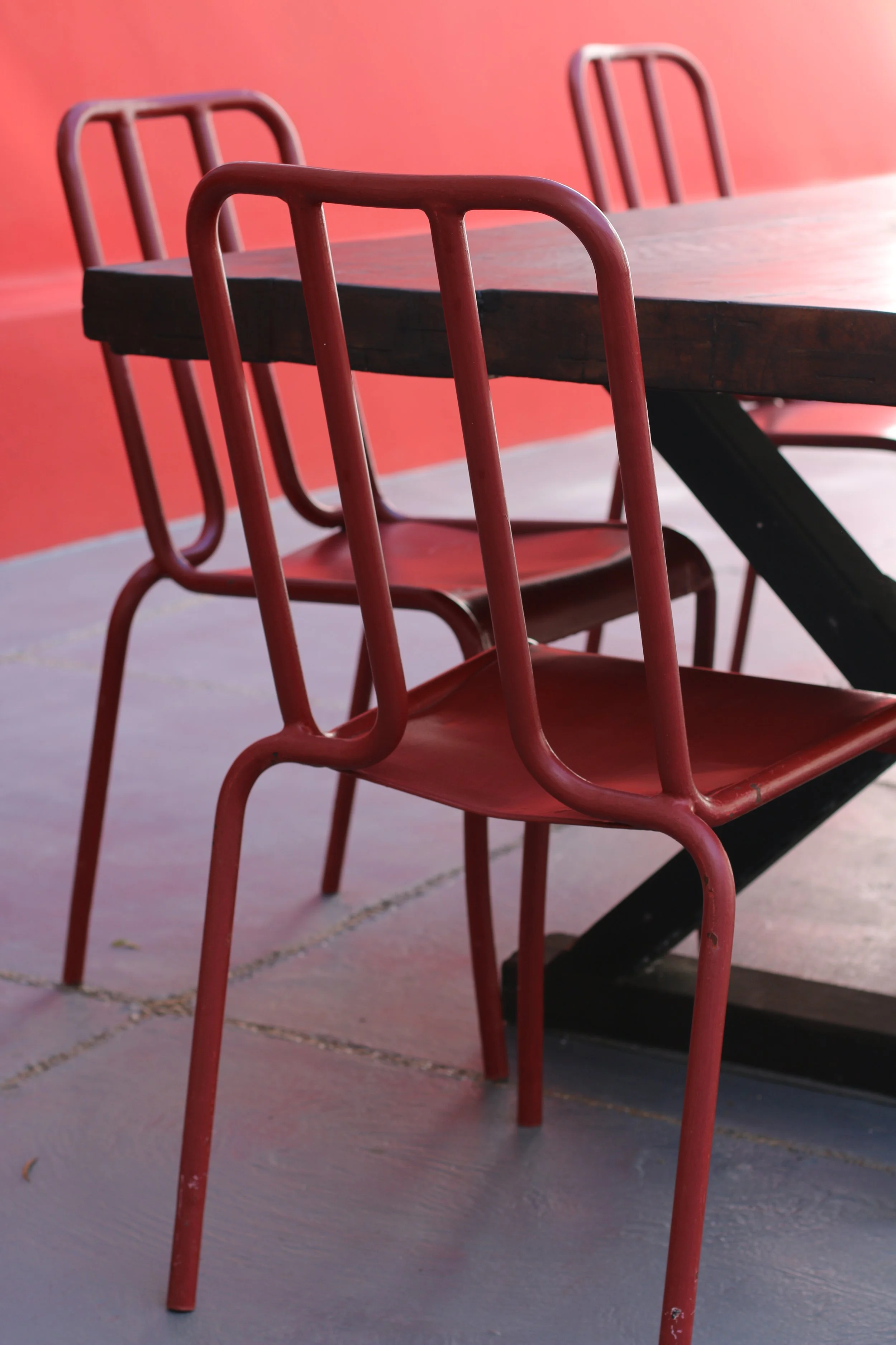 Chaise en métal rouge devant une table en bois avec une paroi rouge en arrière-plan.