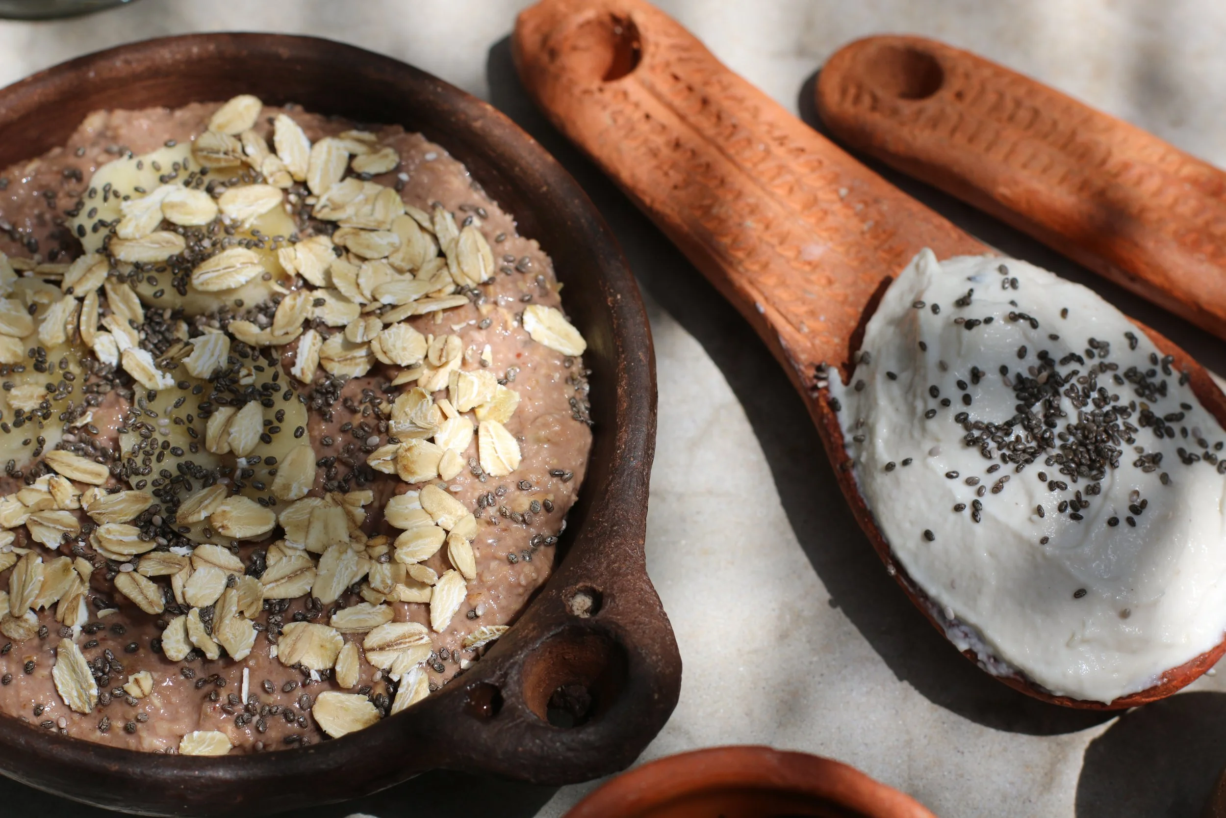 Porridge dans un bol en terre cuite garni de flocons d'avoine, graines de chia et bananes, avec des cuillères en bois à proximité.