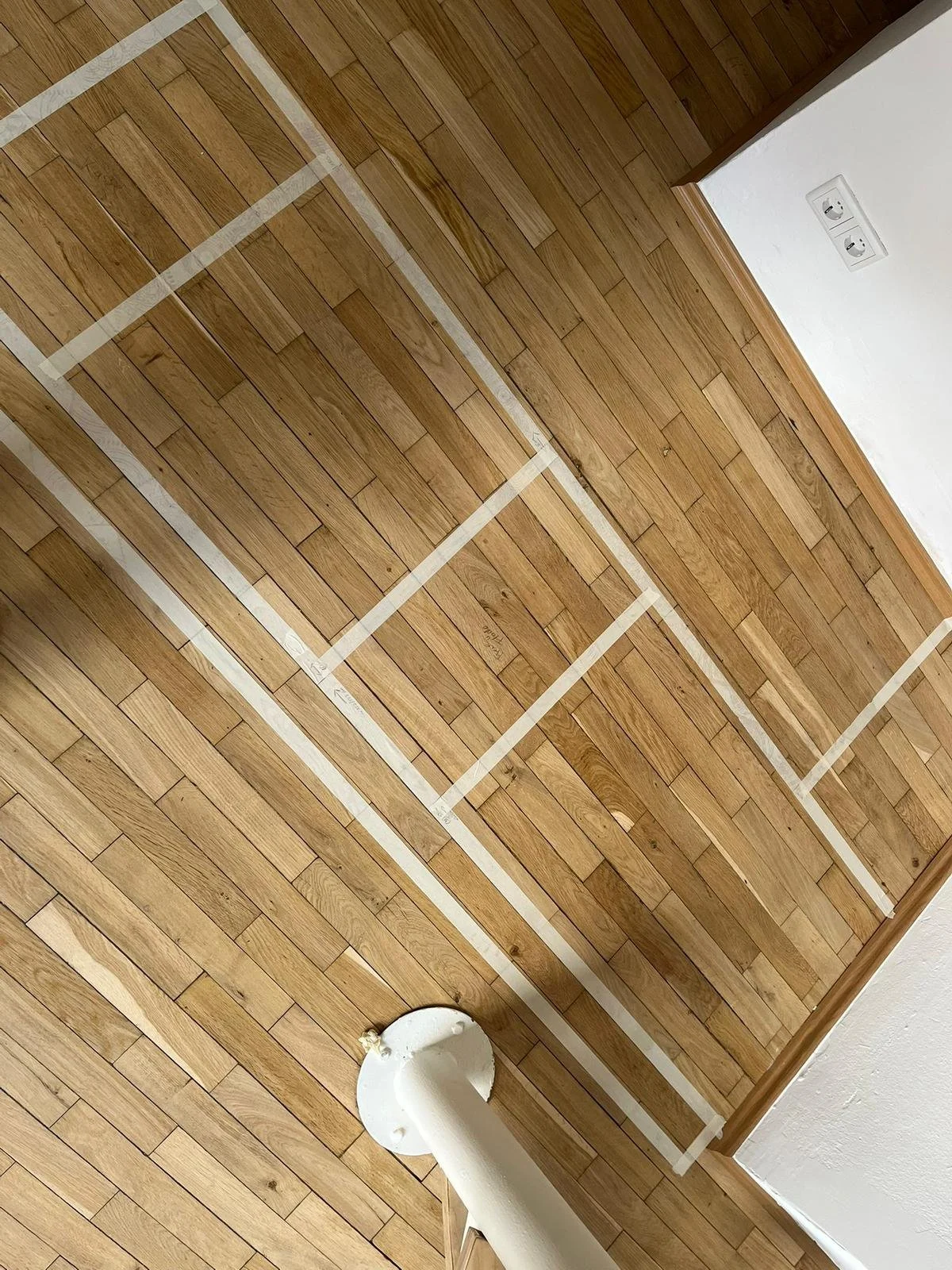 Holzboden mit weißen Markierungen und ein Stützrohr am unteren Rand.