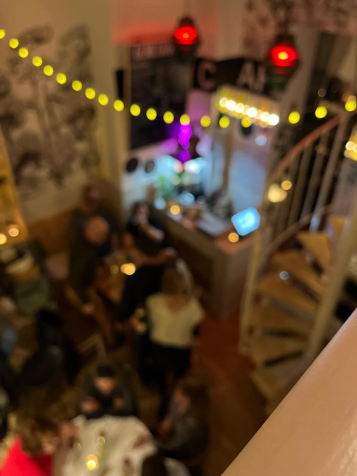 Ein verschwommenes Bild zeigt eine Gruppe von Menschen, die in einem gemütlichen Raum sitzen, geschmückt mit Lichterketten und dekorativen Elementen, vermutlich bei einer Party oder einem geselligen Zusammenkommen.