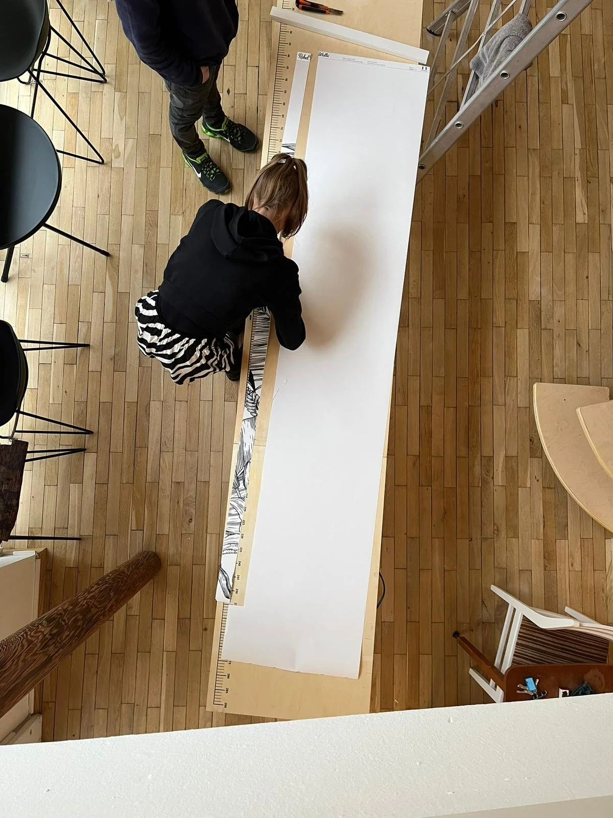 Zwei Kinder beim Basteln an einem langen weißen Papier, auf einem Tisch mit Linealen.