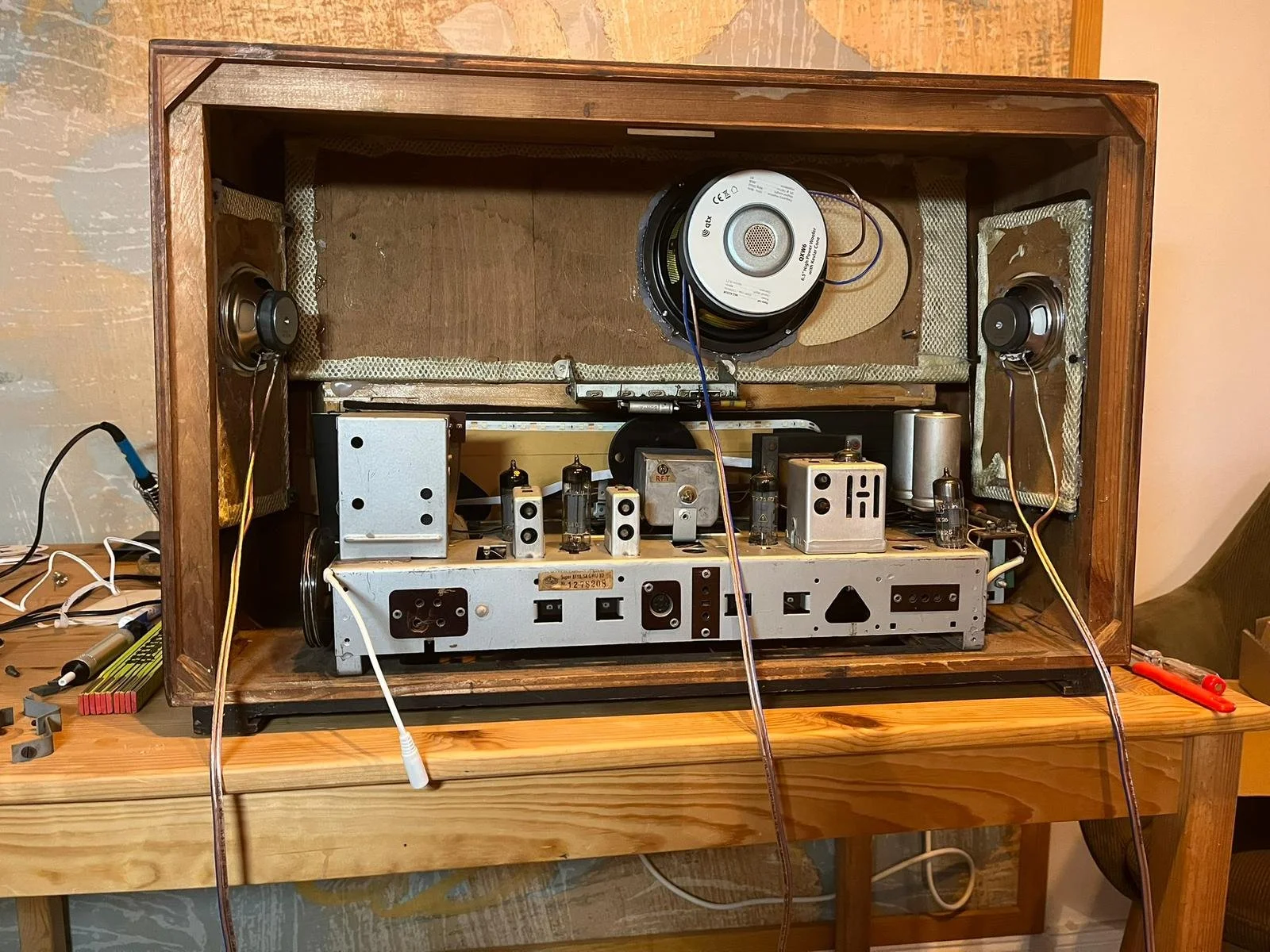 Das Innere eines alten Verstärkers oder Radios, sichtbar sind zwei Lautsprecher, röhrenförmige Bauteile, elektrische Komponenten, Kabel und Werkzeuge auf einem Holztisch.