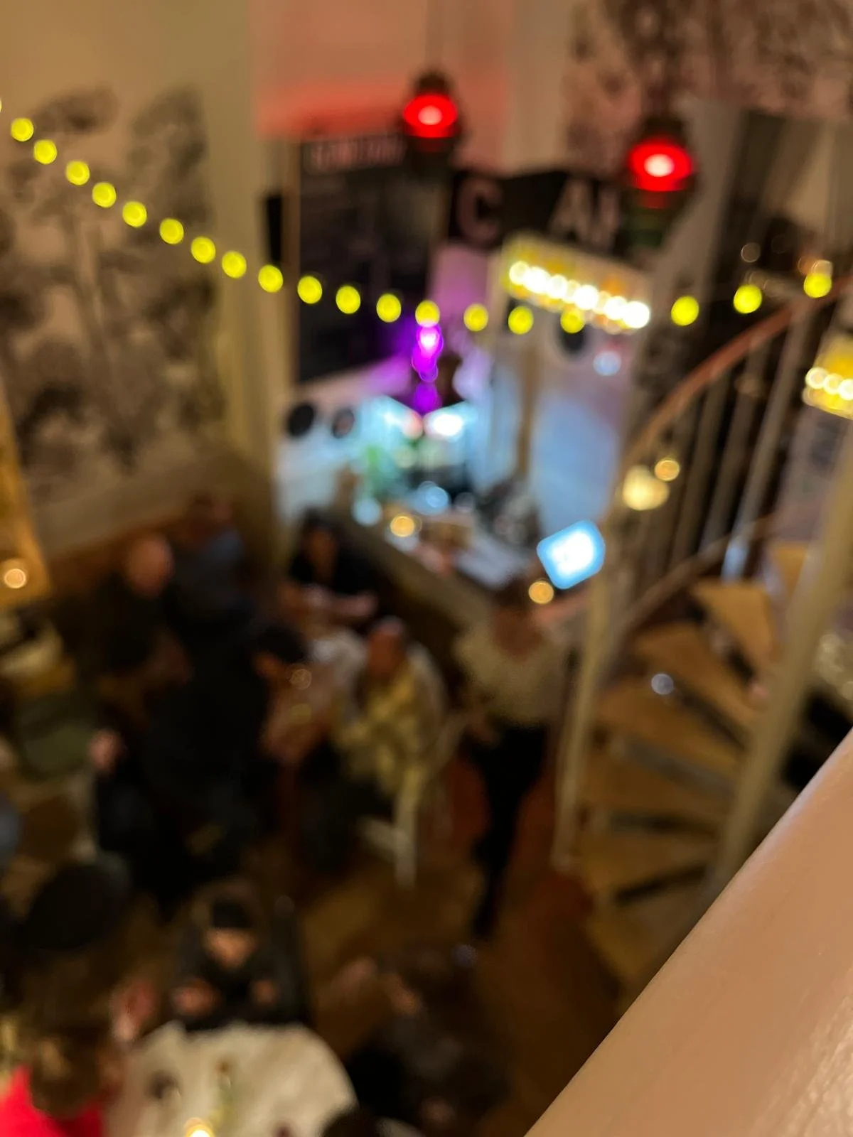 Verschwommenes Bild eines gemütlichen Raums mit Personen, die an einem Tisch sitzen, Lichterketten und einem Fernseher im Hintergrund.