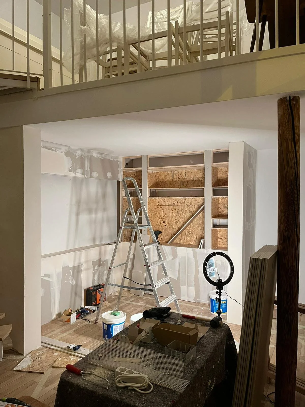 Innenraum eines Hauses unter Renovierung mit Bauwerkzeugen, Leiter und Baumaterialien, teilweise renovierte Wände und offene Holzregale