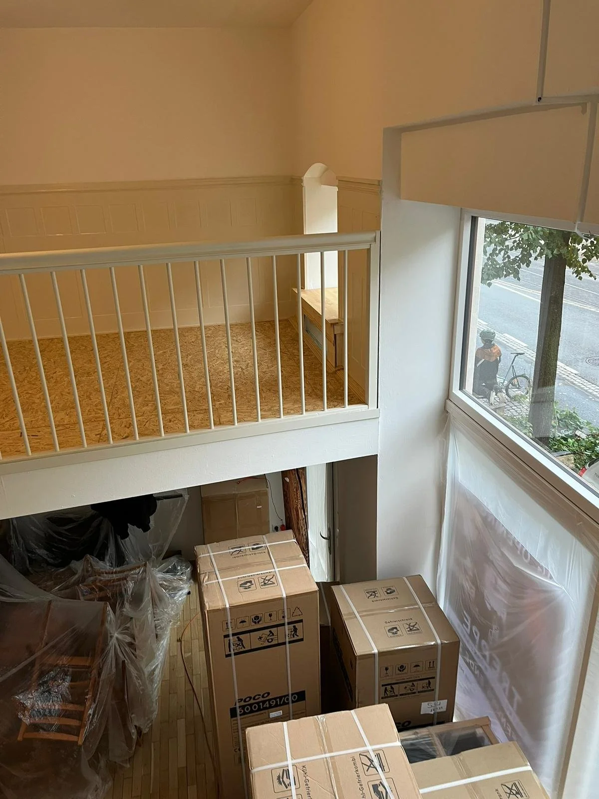 Innenaufnahme eines Raums mit einem Hochbalken, großen Fenstern und mehreren verpackten Kartons.