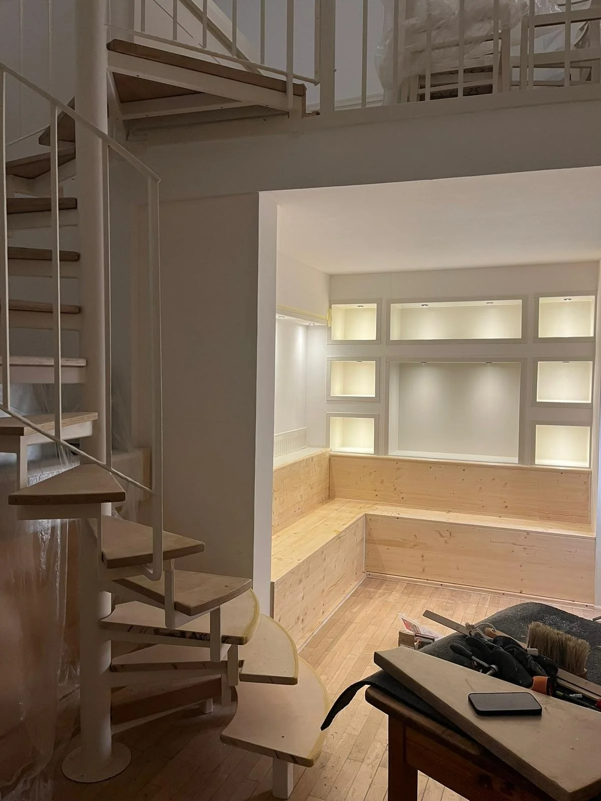 Innenraum eines Hauses mit einer Holzbank, einer Treppe und einer Wand mit Beleuchtungsnischen.