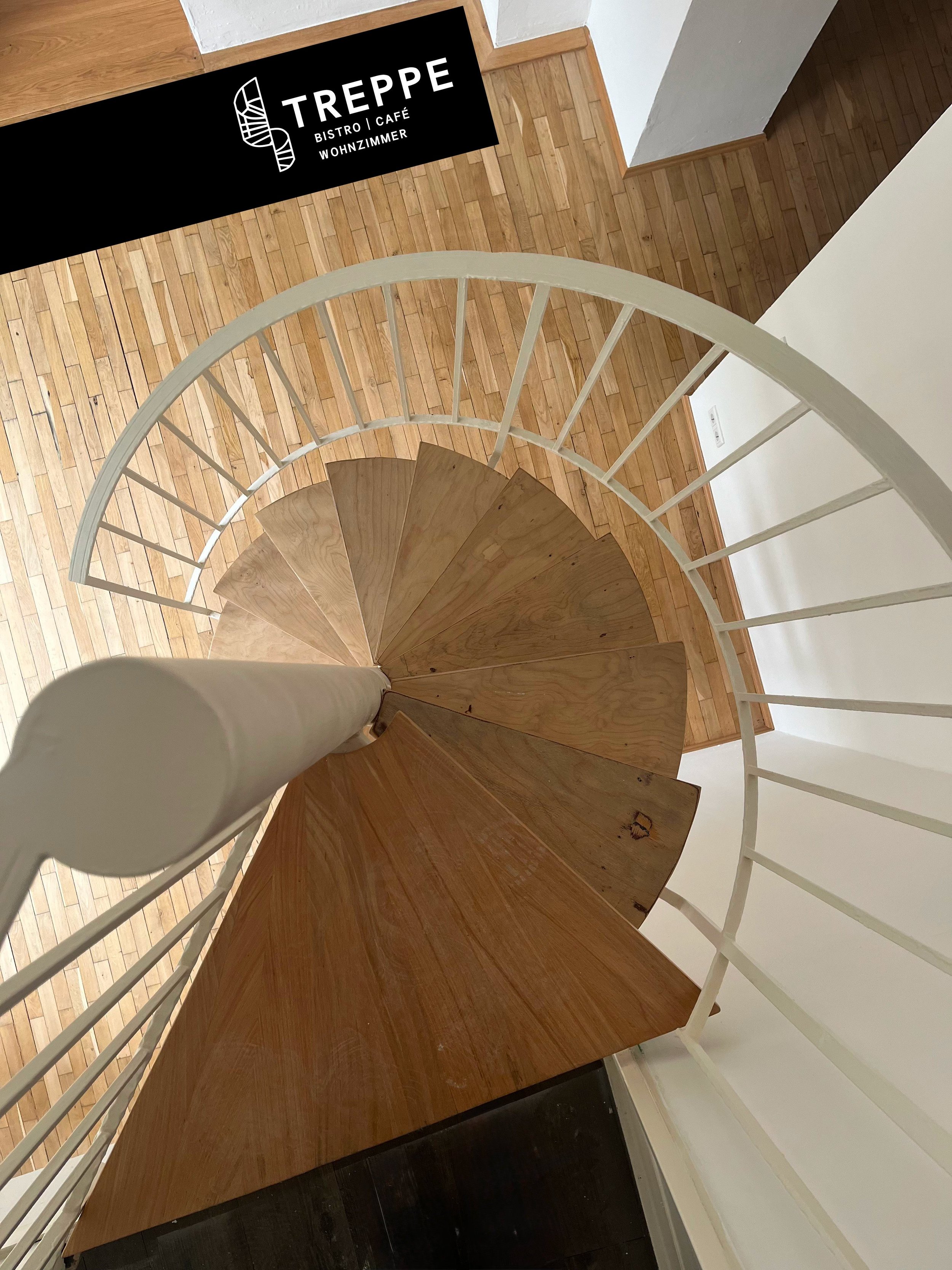 Spiralförmige Holztreppe mit weißem Geländer in einem Gebäude, Blick von oben nach unten.