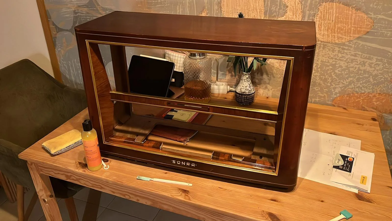 Retro-Schallplattenspieler auf einem Holztisch, umgeben von Papierdokumenten, Reinigungswerkzeug und einer Flasche mit Reinigungsflüssigkeit.