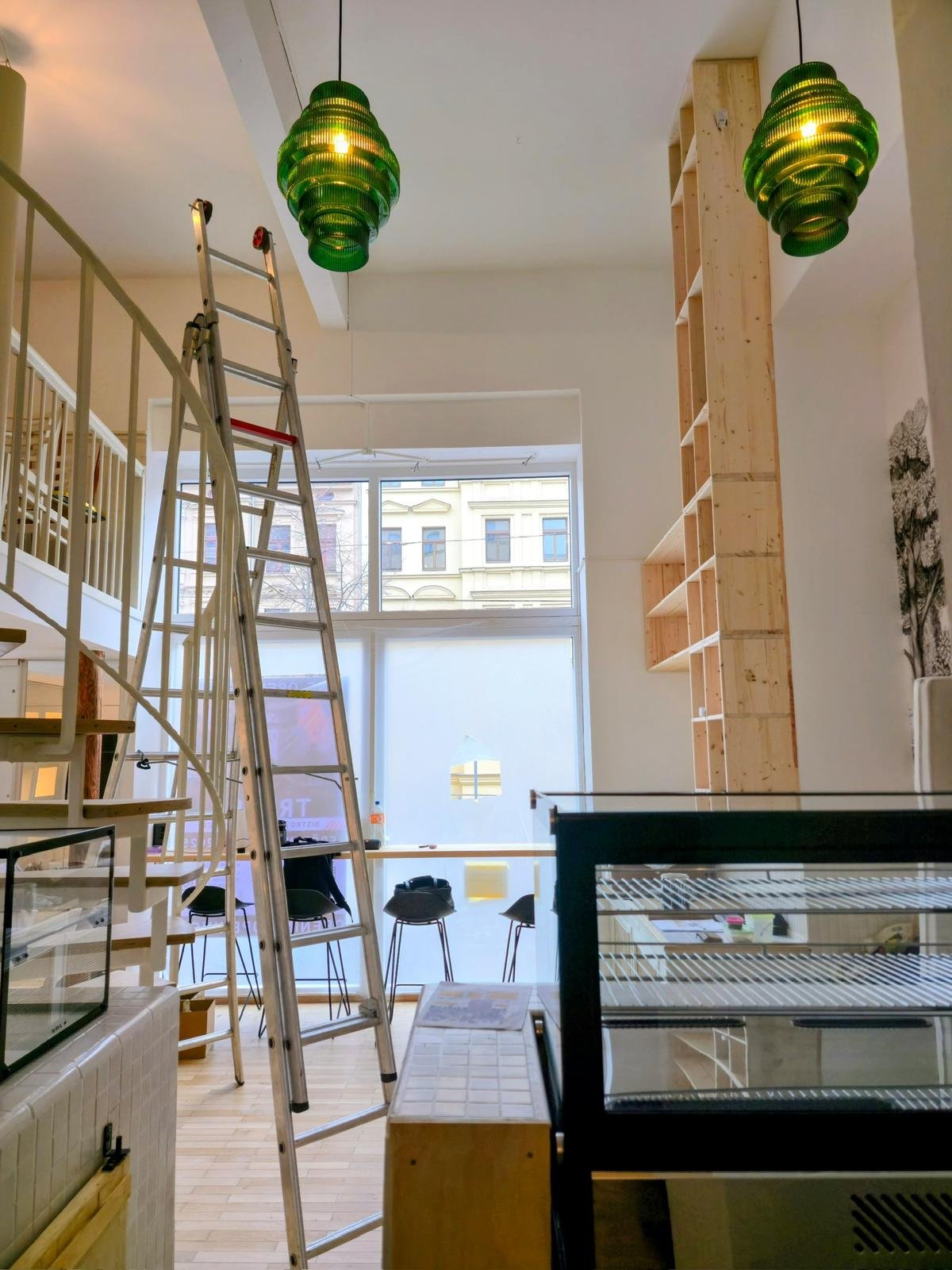Innenansicht eines Cafés oder Restaurants im Umbau, mit Leiter, Barhockern, Verkaufsregal und grünen Lampen.