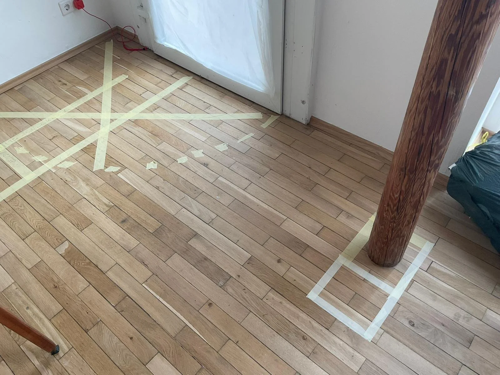 Der Boden im Raum ist mit Klebeband markiert, wahrscheinlich für Renovierungs- oder Reparaturarbeiten, mit einer Holzstützsäule im Raum.