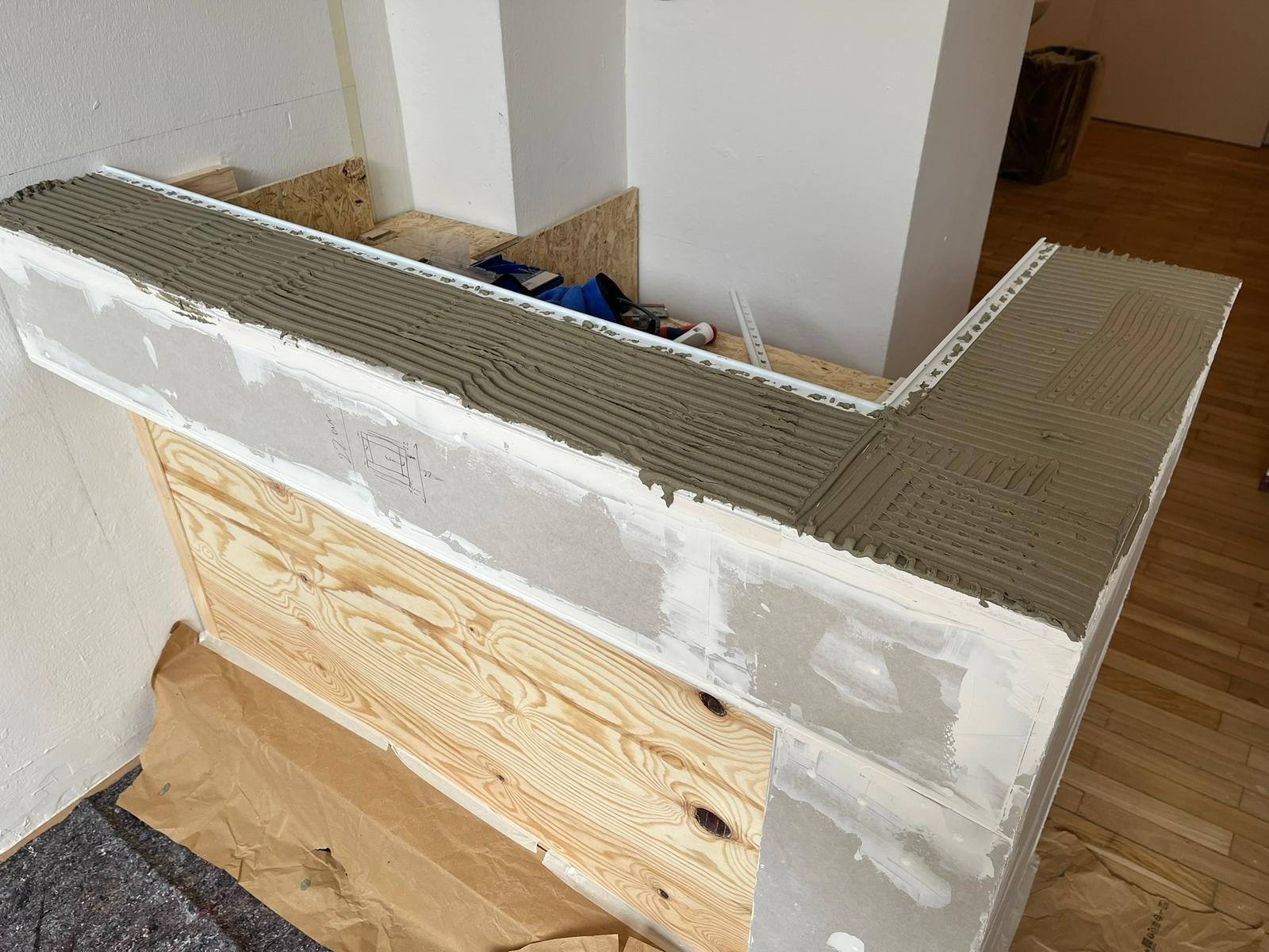 Ein halb fertiger Wandaufsatz mit Lehmputz und Sitzbank, mit Werkzeugen und Holzplatten auf den Flächen.