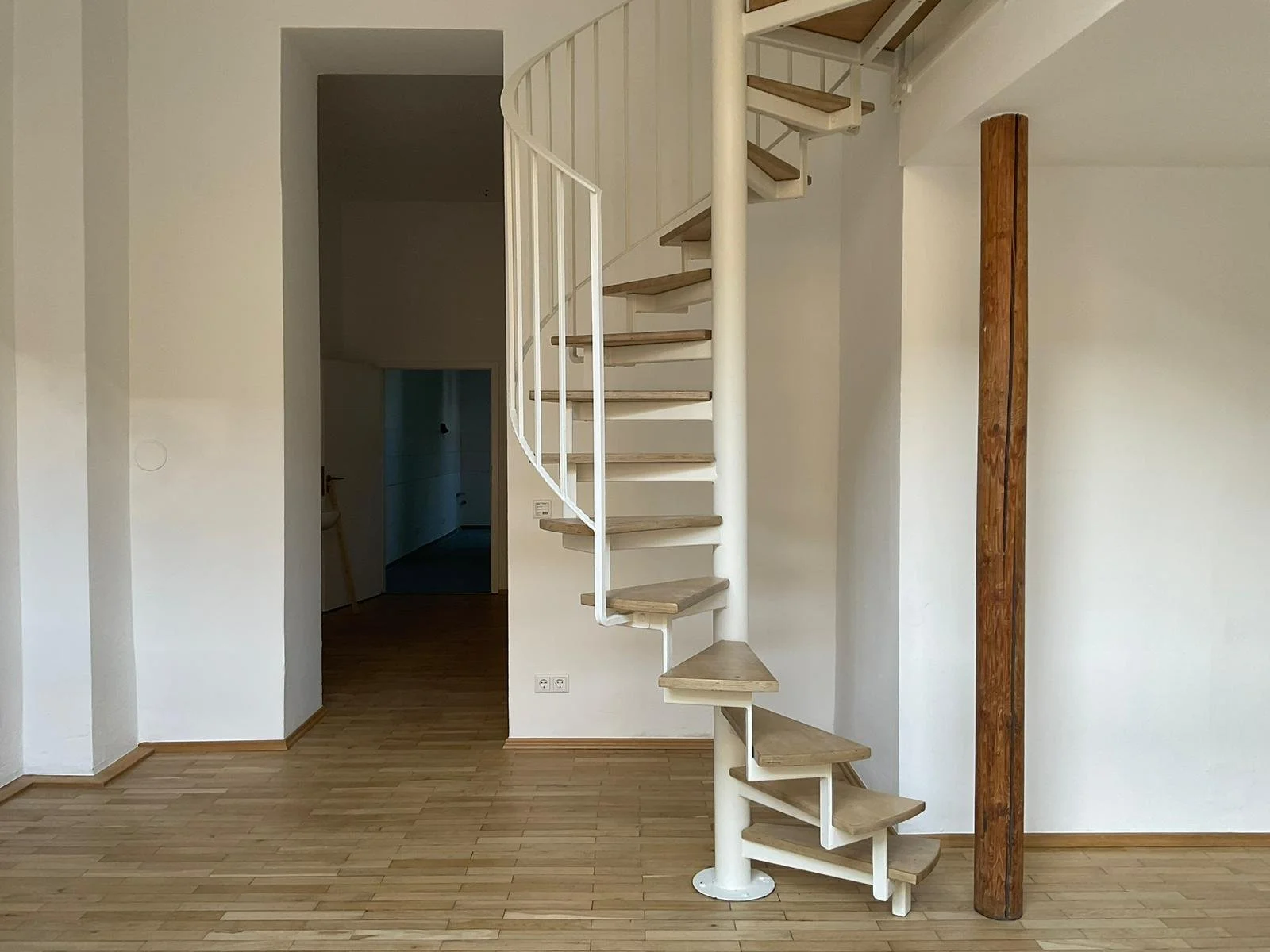 Innenraum mit einer weißen Spiraltreppe, Holzstufen und einem Holzbalken an der Wand