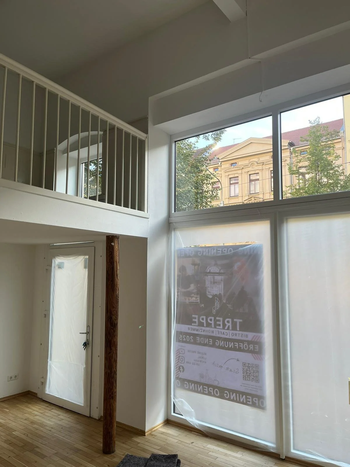 Innenraum eines Hauses mit hohen Decken und großen Fenstern, eingerüsteter Tür und einer Holzstütze.