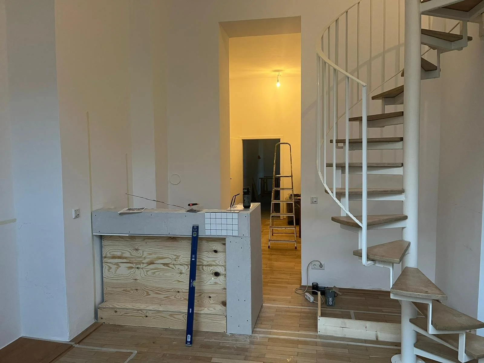 Innenraum eines Hauses im Bau. Es gibt eine halb fertige Kücheninsel, eine Treppe und eine bewölkte Wand—alles im Rohzustand.