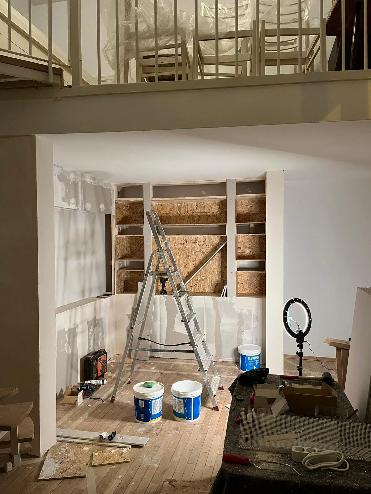Innenaufnahme eines Raumes im Renovierungszustand mit einer Leiter, Baustoffen, Werkzeugen und unvollständigen Wandregalen.