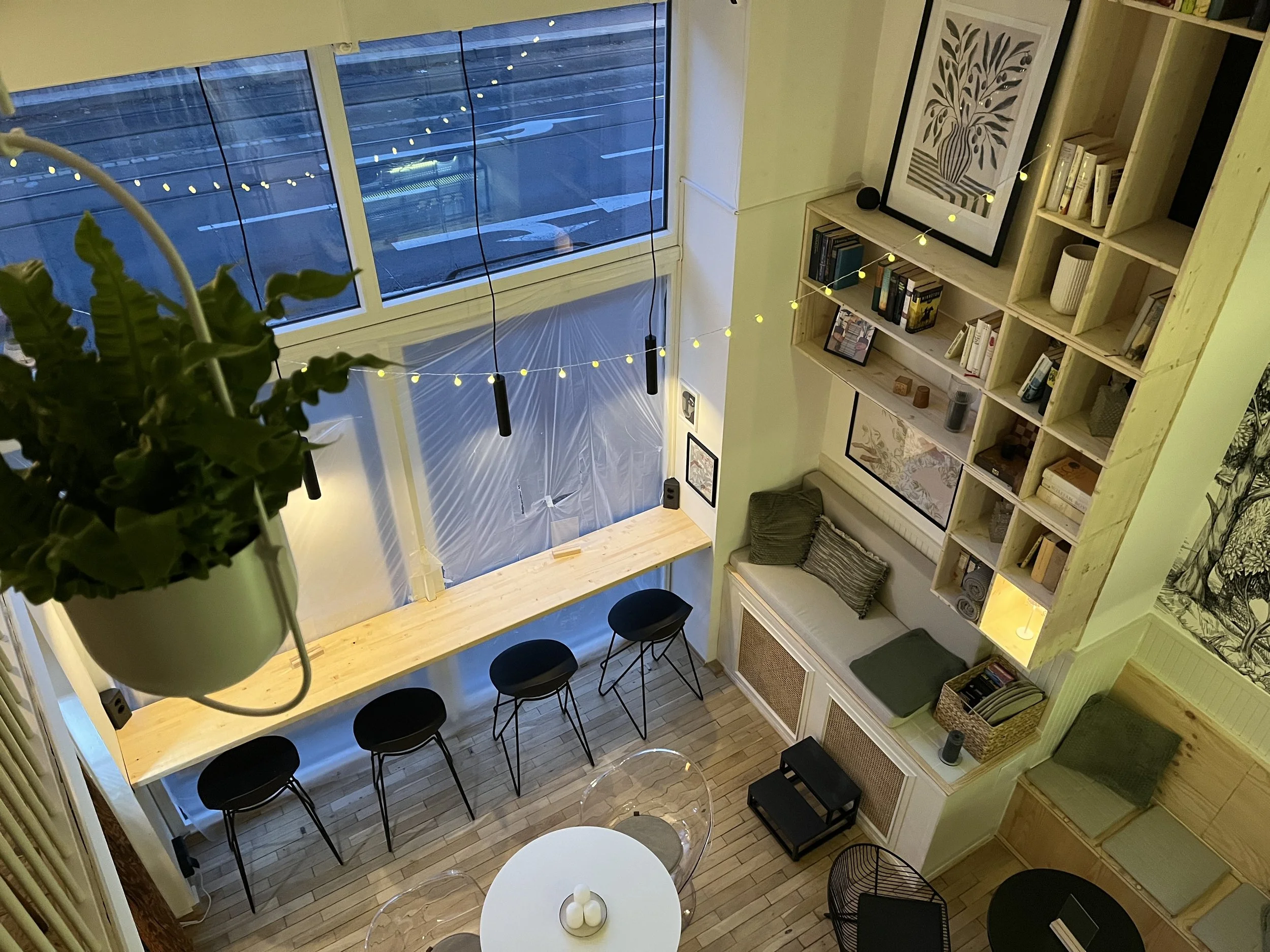 Ein Blick nach oben in ein Wohnzimmer mit großem Fenster, Bücherregal, Sitzgelegenheiten und Beleuchtung.