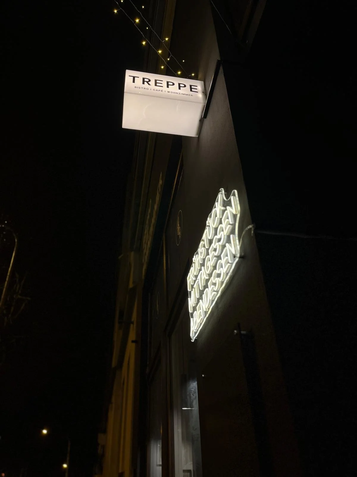 Schriftzug mit dem Wort 'TREPPE' auf einem beleuchteten Schild sowie eine Neon-Reklame in Schreibschrift