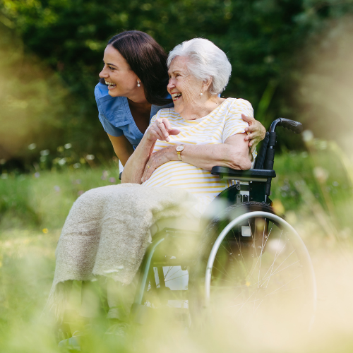 An in-home caregiver smiling with an elder woman in her garden as she ages in place peacefully and safely