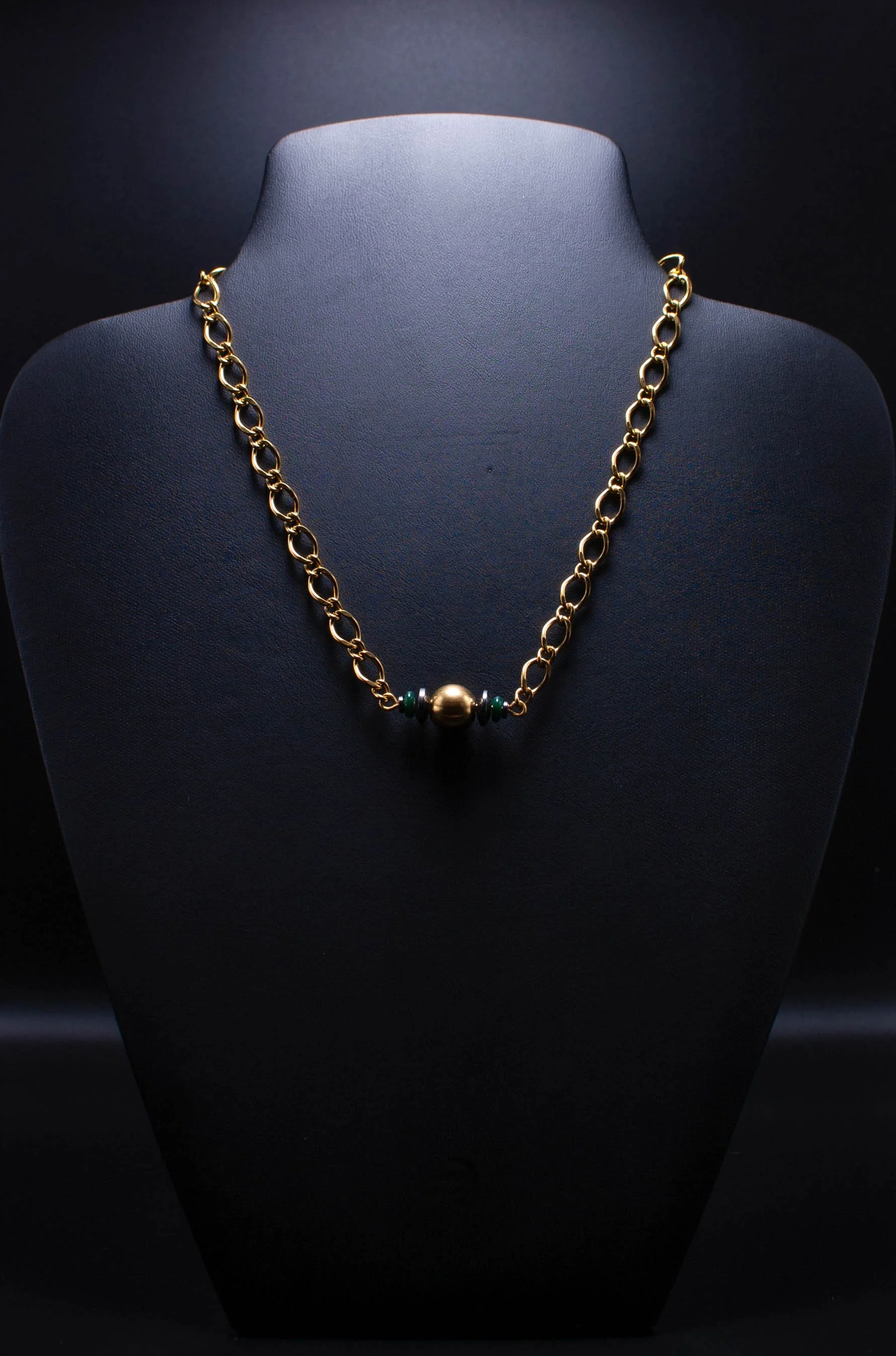 Gold chain necklace with a large central bead and smaller green beads on a black display bust.
