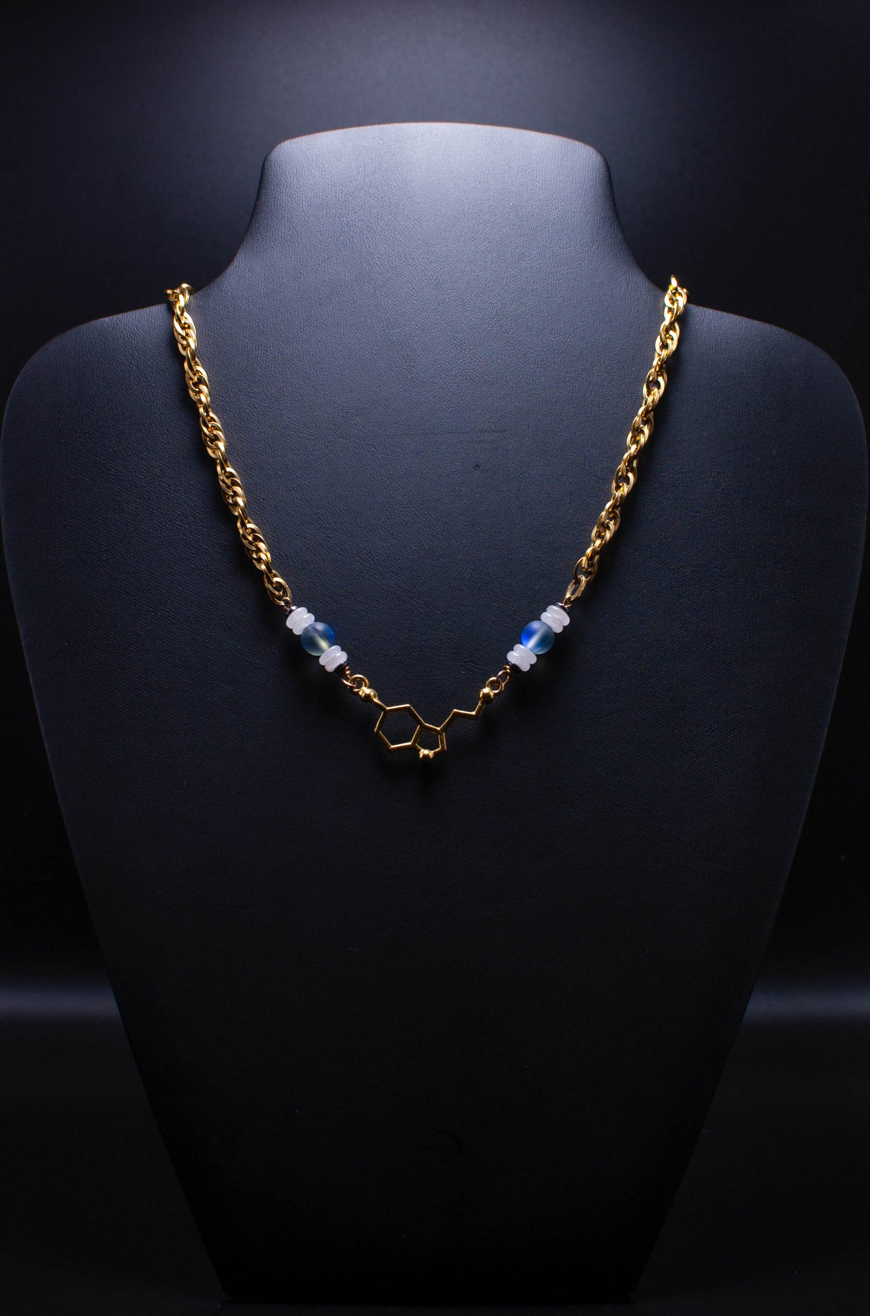 Gold necklace with a molecular structure pendant, displayed on a black jewelry stand.