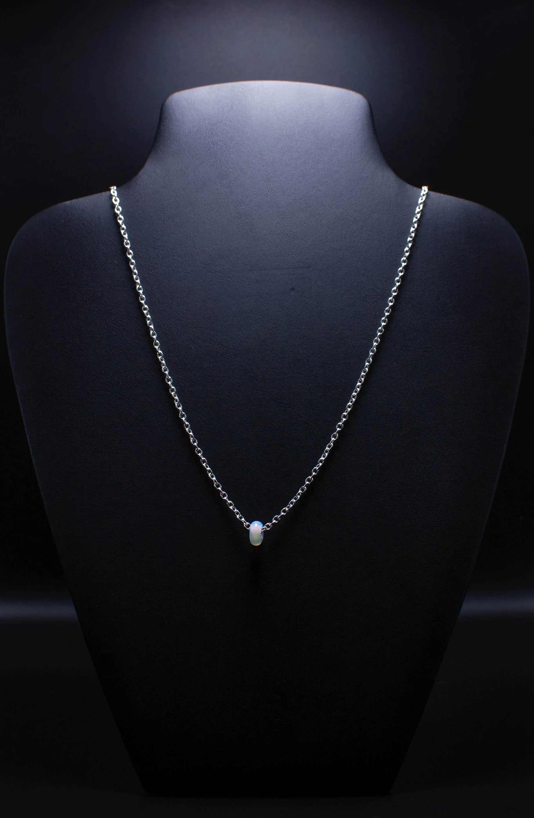 A silver chain necklace with a small white pearl pendant displayed on a black jewelry stand.