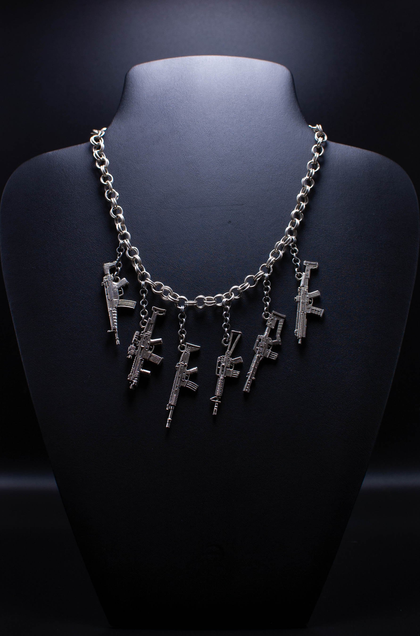 Silver necklace with gun-shaped pendants hanging from a chain, displayed on a dark necklace bust.