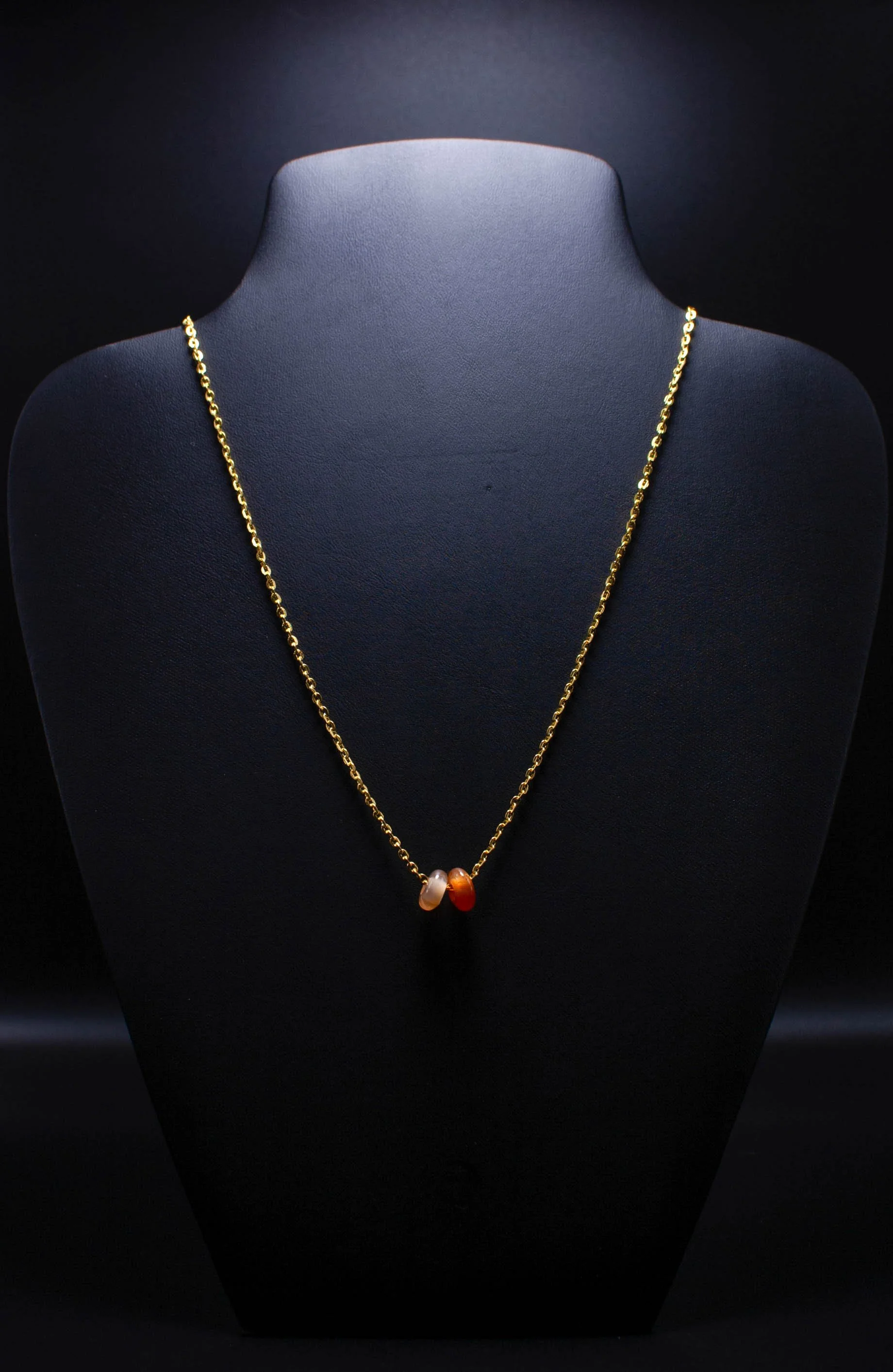 Gold necklace with three colored stones on black display bust.