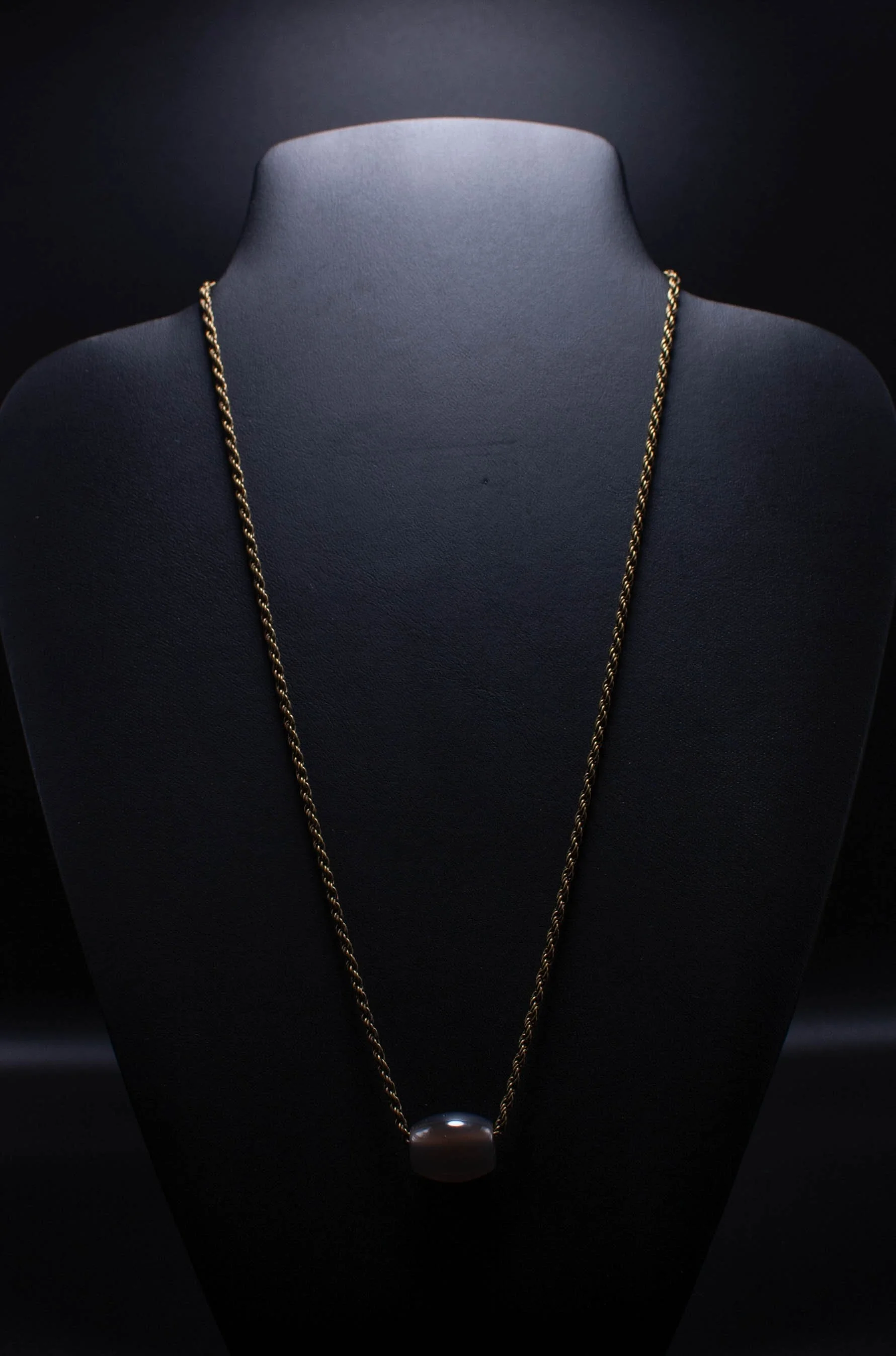 Gold chain necklace with a large pearl pendant displayed on a black jewelry bust.