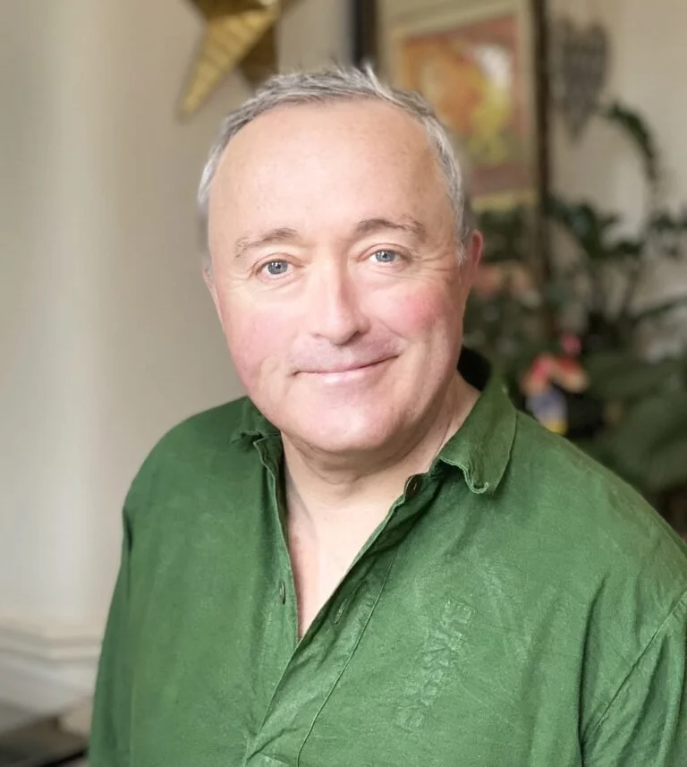 An actor for Don't Mind Cruxmont, a mystery fiction podcast. A man in a green buttoned shirt with short white hair and a friendly smile.