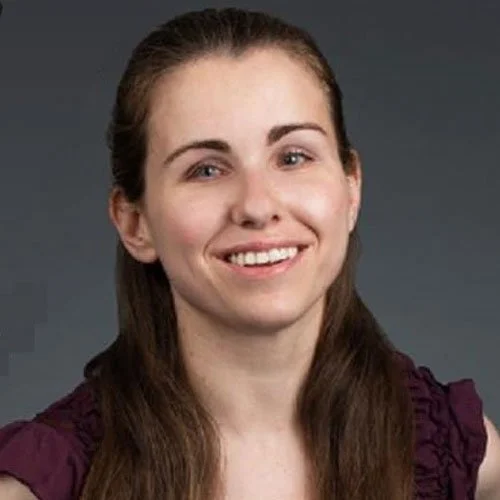 A voice actor from The Boar Knight, an all-ages fiction podcast. A smiling woman with long brown hair and a purple top with ruffles. She has green eyes and its clear that she's a very good voice actress.