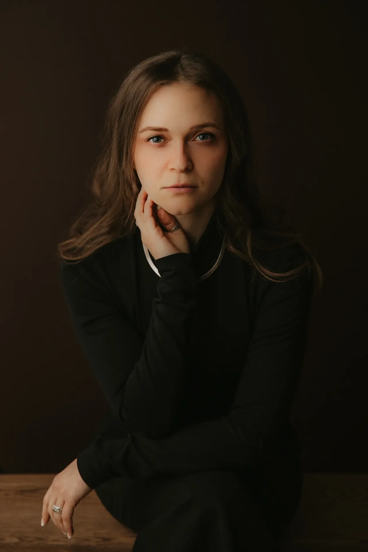 A woman in a black sweater with long dark hair and intense eyes. One hand touches her chin and she's wearing a silver ring on her thumb.. K.A. Statz of Fool & Scholar Productions. A horror fiction writer for audio drama..