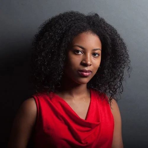 An actor from Liberty: Tales from the Tower, a horror fiction podcast. A woman with voluminous shoulder-length black hair wearing a red dress.