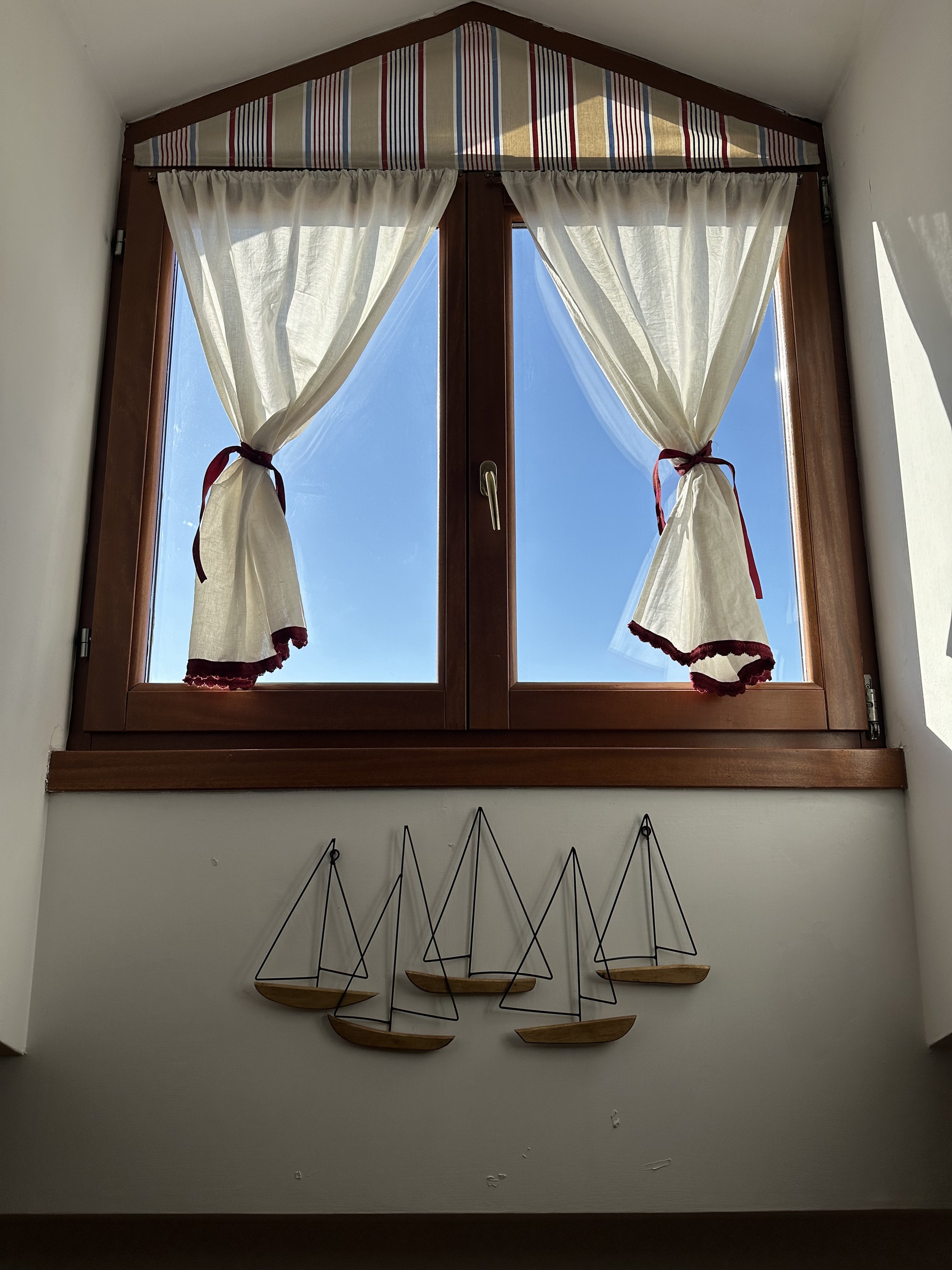 Finestra con tende bianche legate lateralmente, finestra in legno con interno blu cielo.