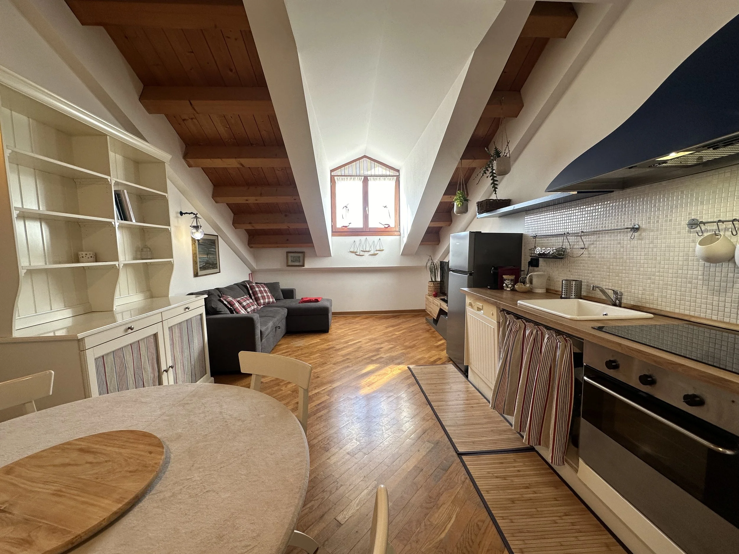 Interno di un attico con cucina a sinistra, soggiorno con divano nero e soffitto con travi in legno, finestra a tetto