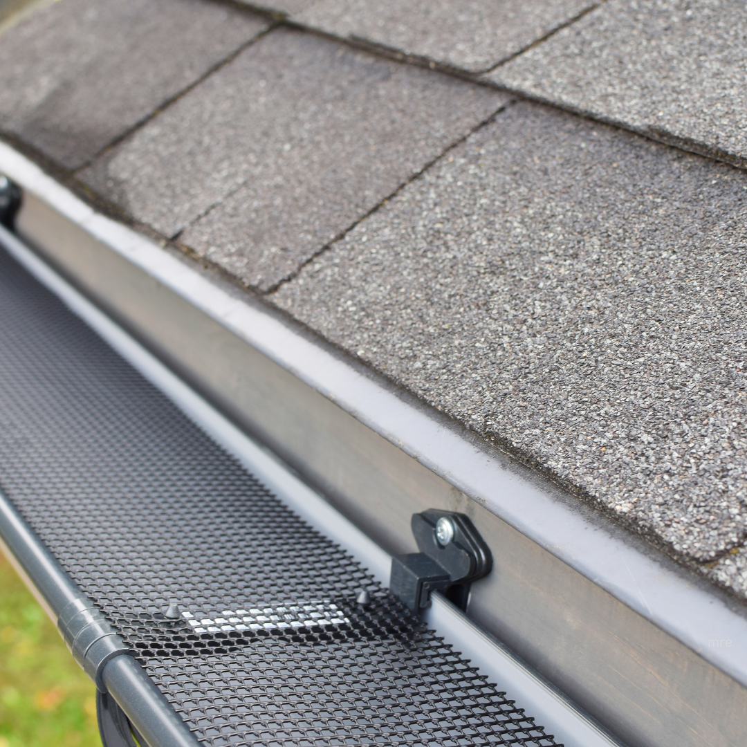 Close-up of a section of residential shingle roof and an attached metal gutter with a small black accessory.
