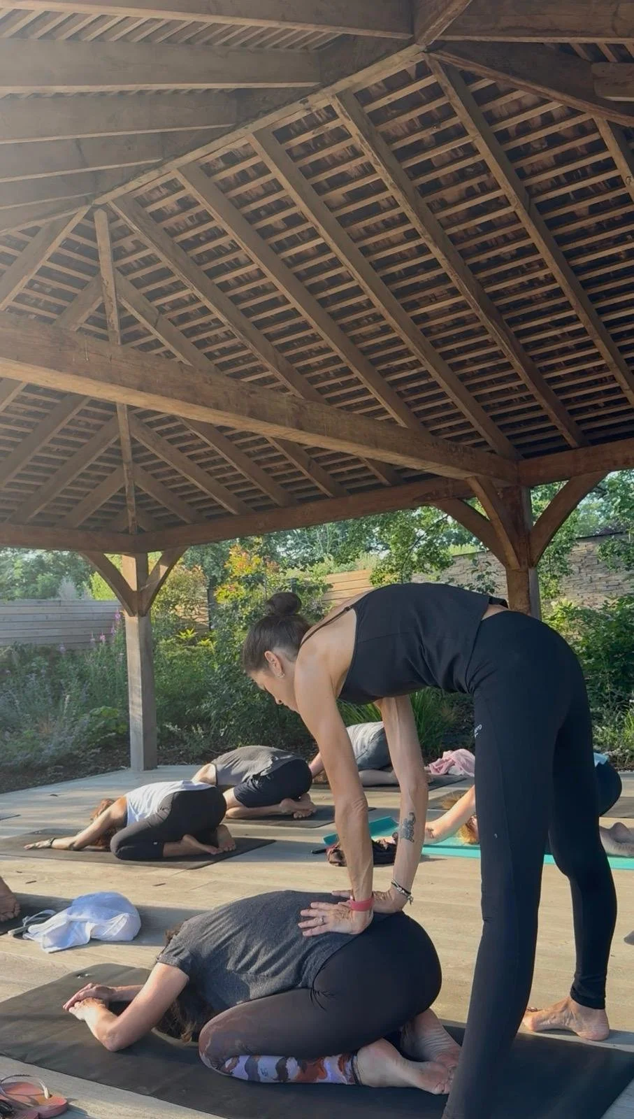 People participating in a yoga class outdoors under a wooden gazebo.