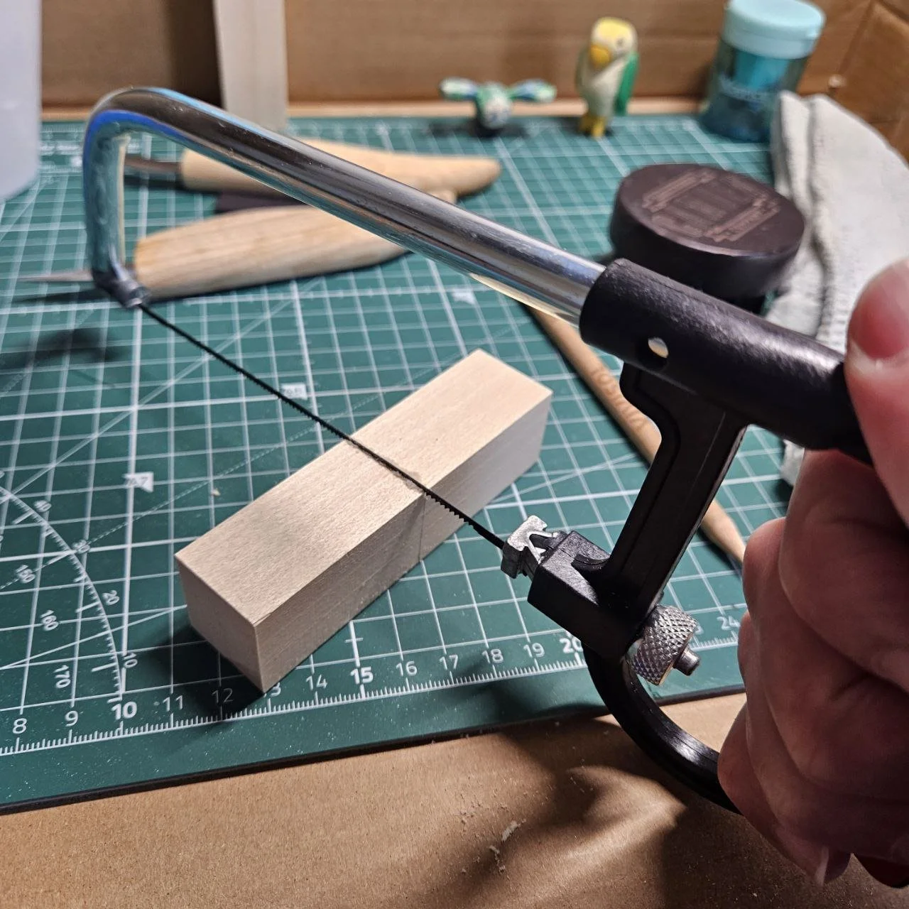 persona che utilizza una sega a mano per tagliare un pezzo di legno su un tappetino da lavoro verde con linee di misura.