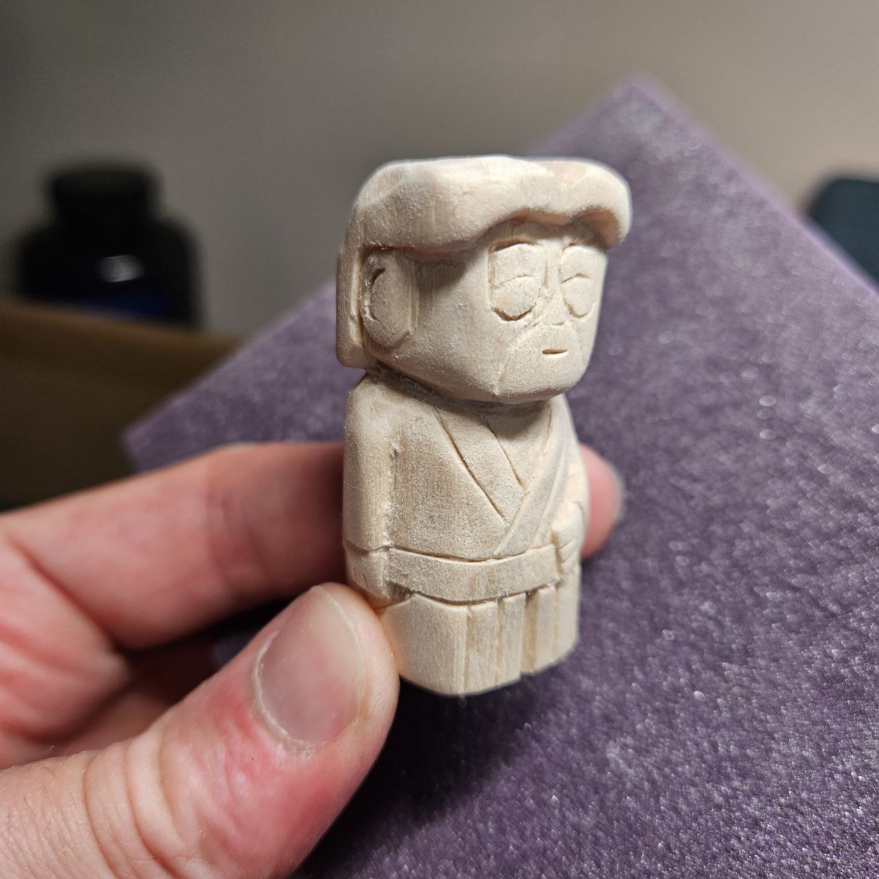 Statua in legno di una figura di stile giapponese, con capelli corti e occhiali, vestita con kimono. La figura è stilizzata e scolpita a mano.