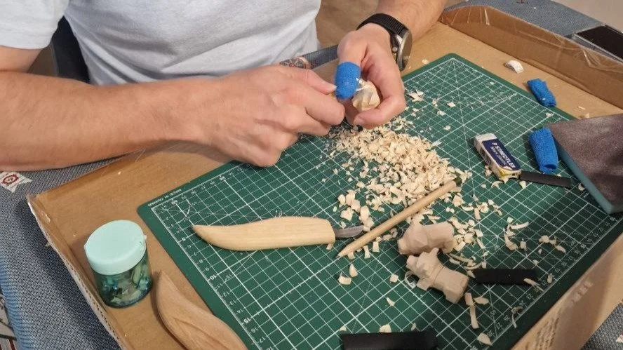 Una persona che lavora su un progetto di falegnameria o modellismo, con vari strumenti e materiali di legno su un tavolo.