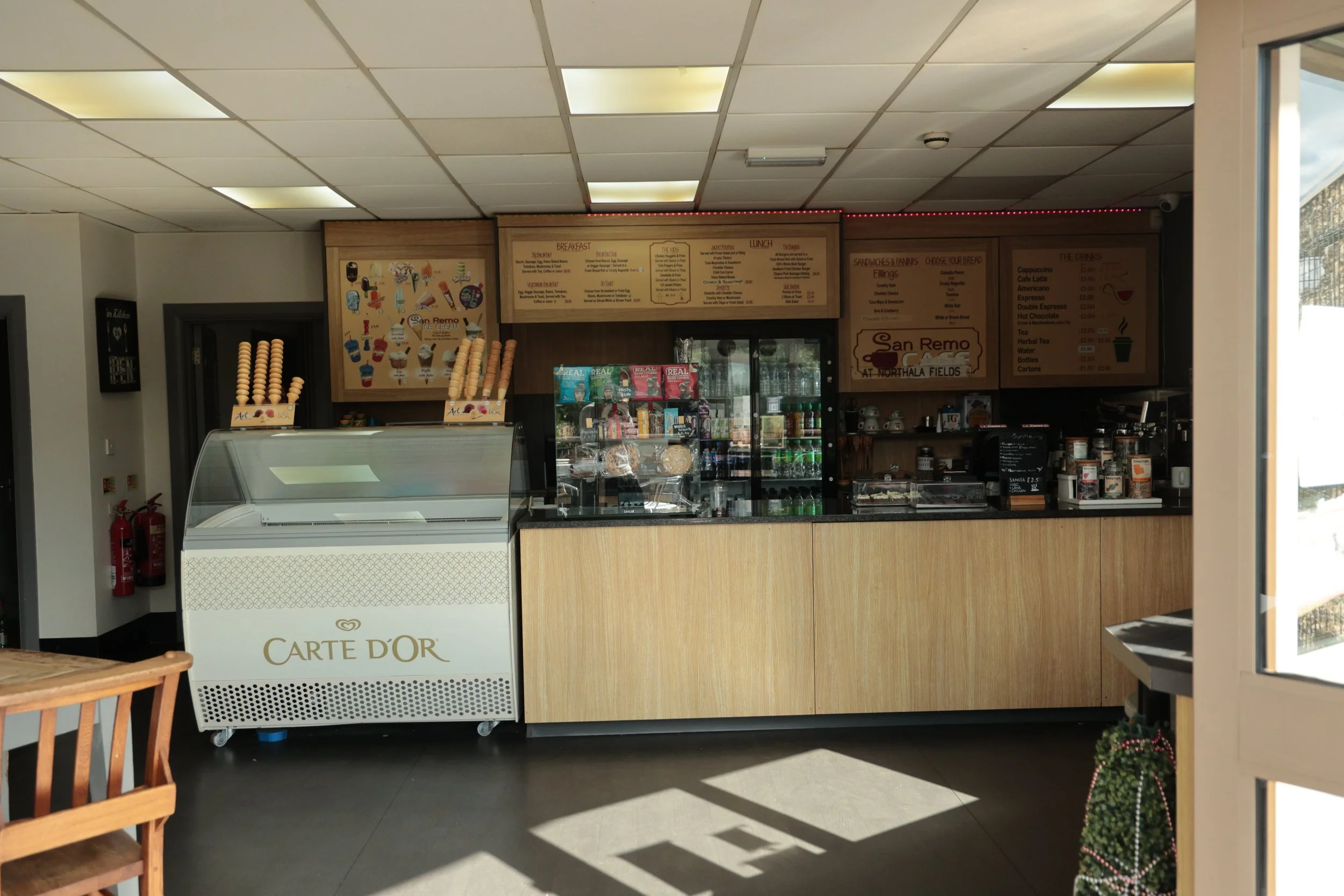 Inside a cafe with a menu board, ice cream freezer labeled 'Carte D'Or', and various drink and snack displays.