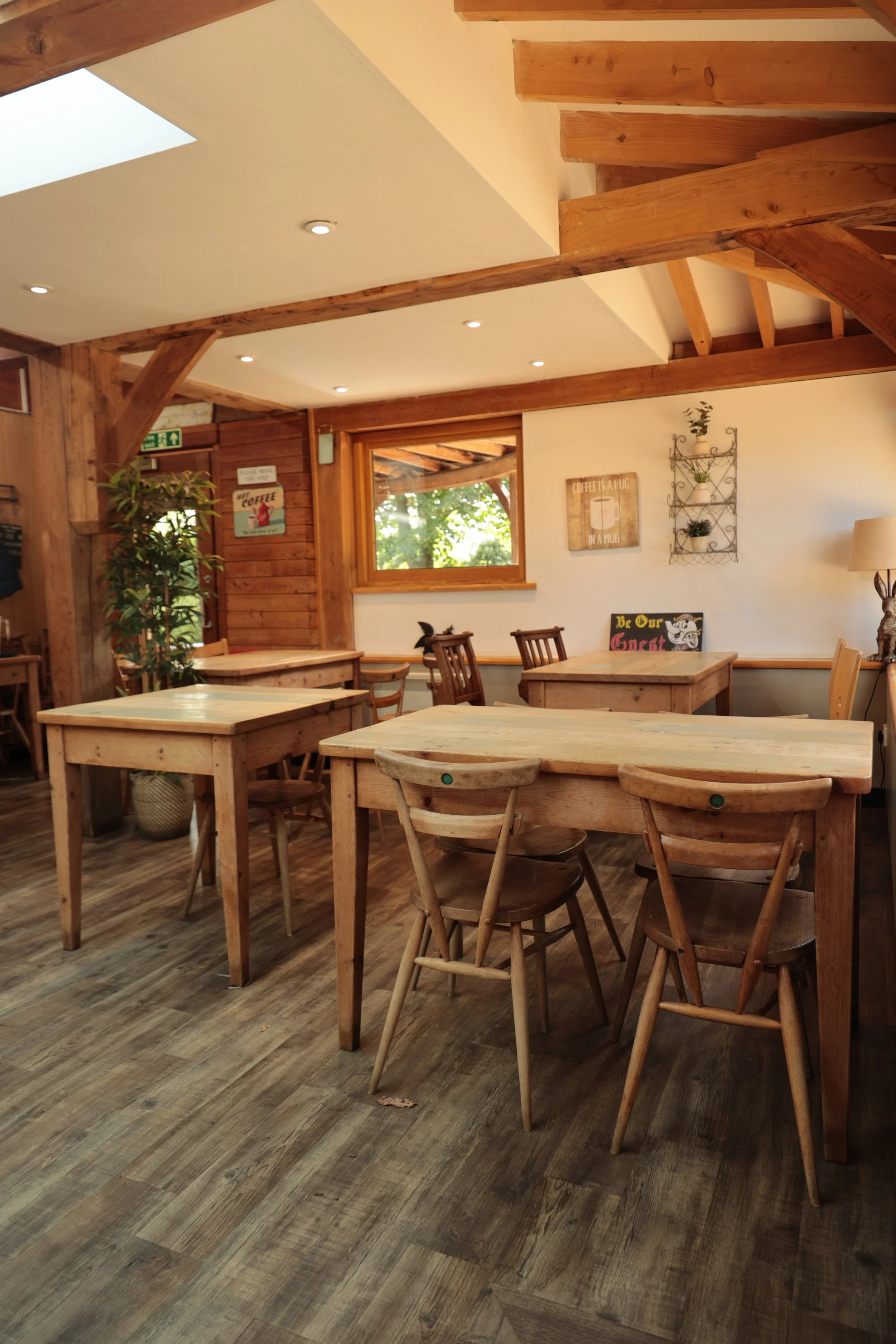 Interior of a cozy cafe with wooden tables and chairs, a wooden wall, plants, and decorative signs on the wall.