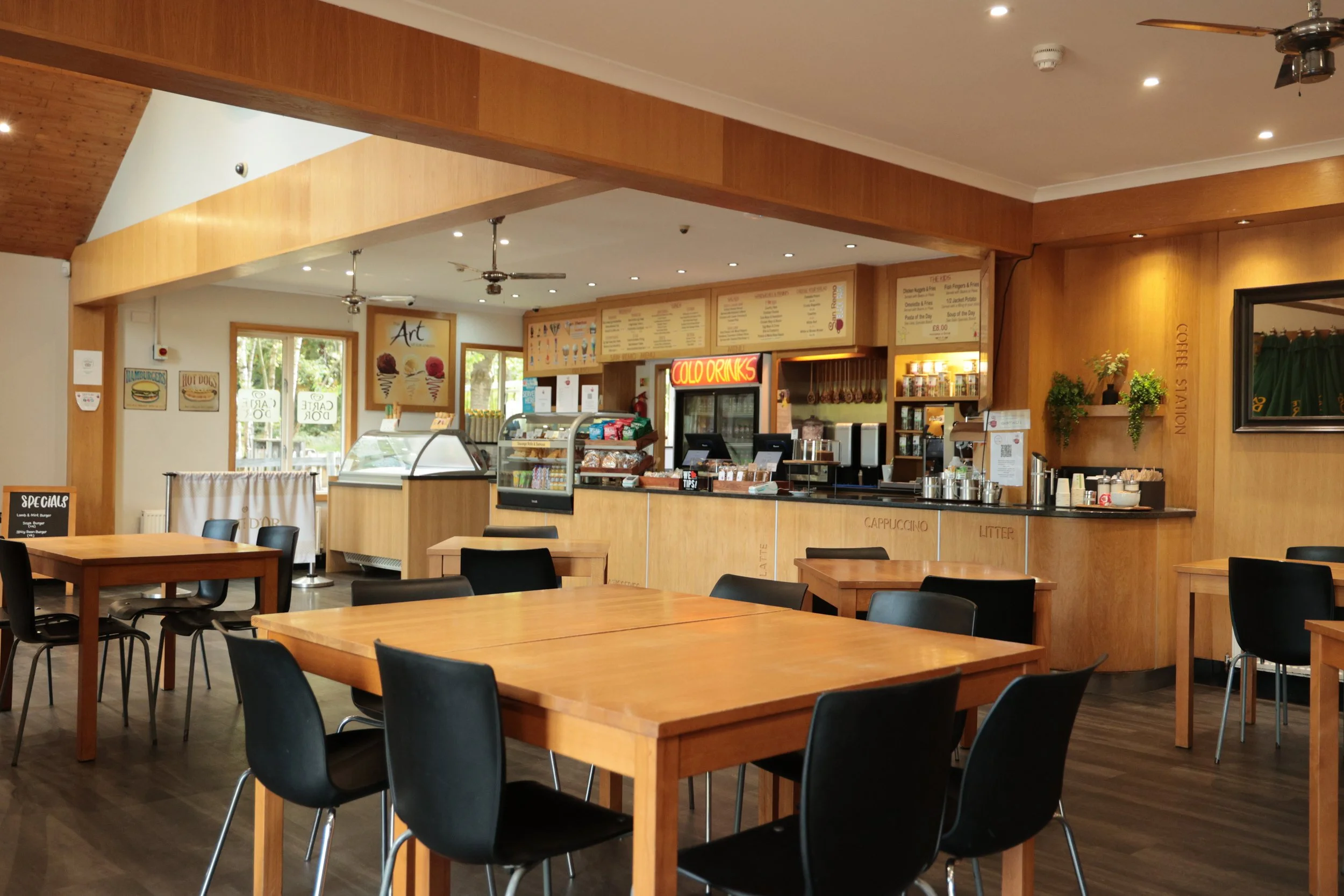 Interior of  shop with wooden furniture, black chairs, and a counter with a menu board and food display.
