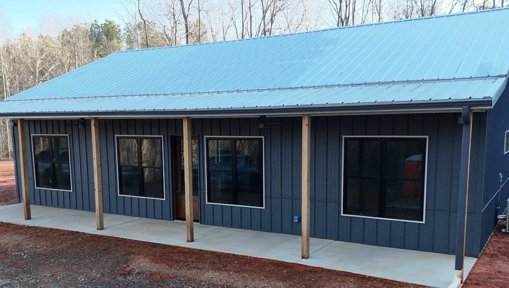 Architect's drawing of a brndominium house with a gable roof, four windows, and a front door, featuring a stone foundation and vertical siding.