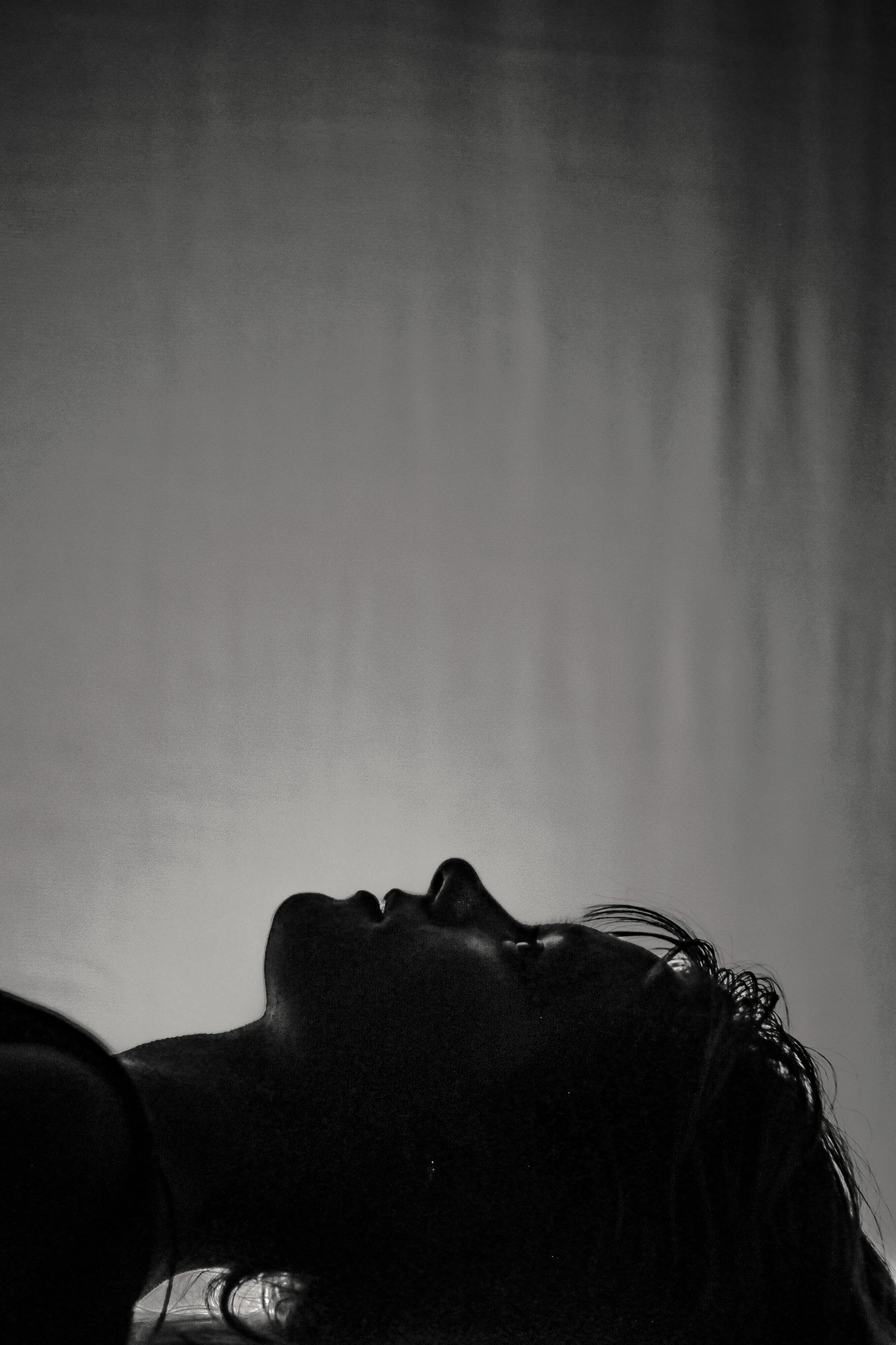 Silhouette of a woman lying down with her head tilted back, dark and shadows, with light falling on her face and hair.