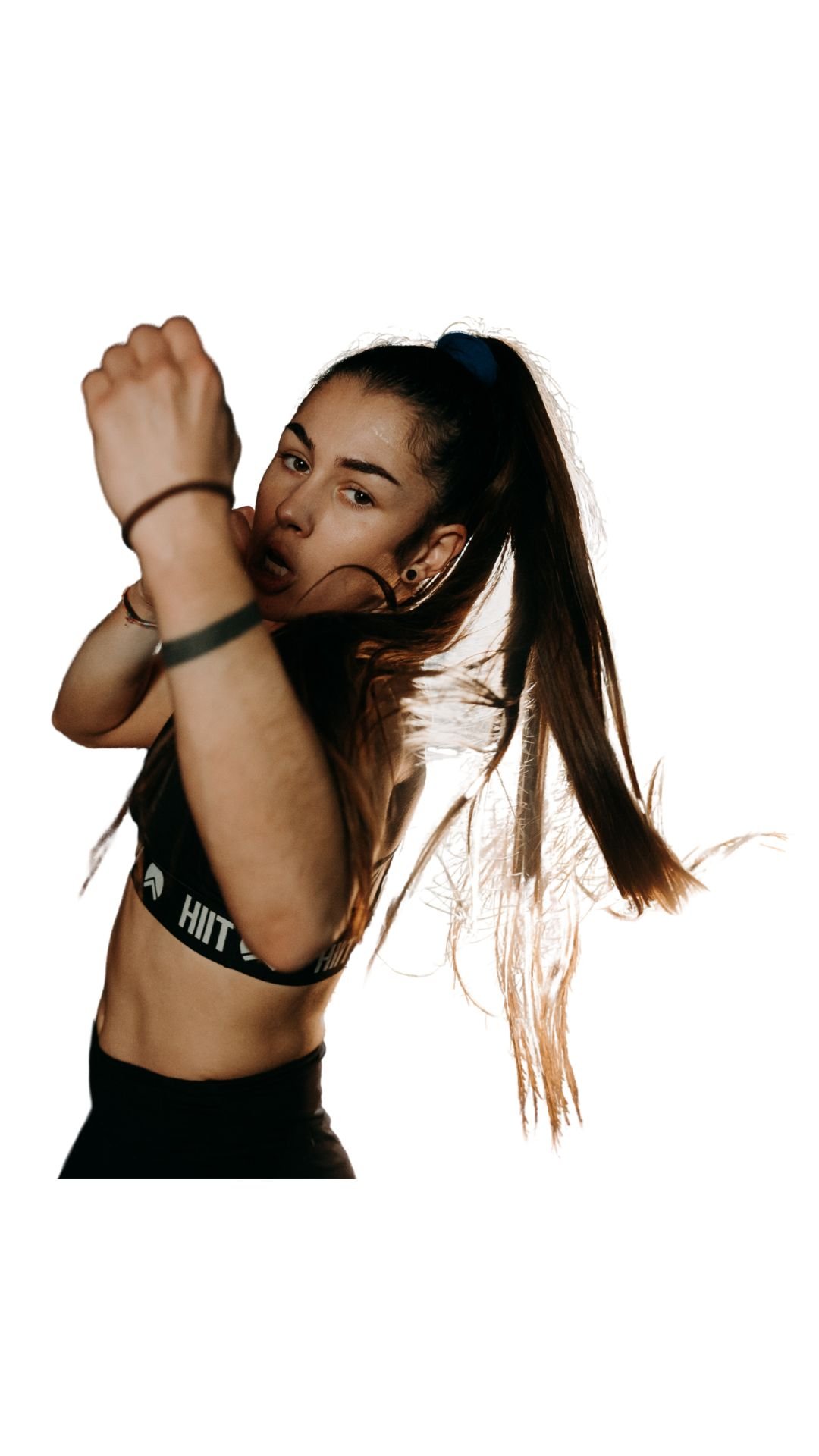Une femme sportive dans une pose de combat, portant un haut de sport noir et des accessoires, avec cheveux longs attachés en queue de cheval, exprimant la détermination.